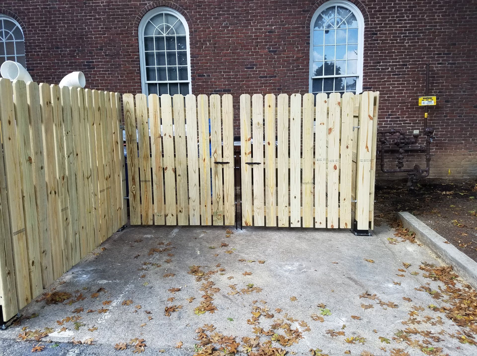 Wooden gate across a small concrete courtyard beside a brick building with arched windows.