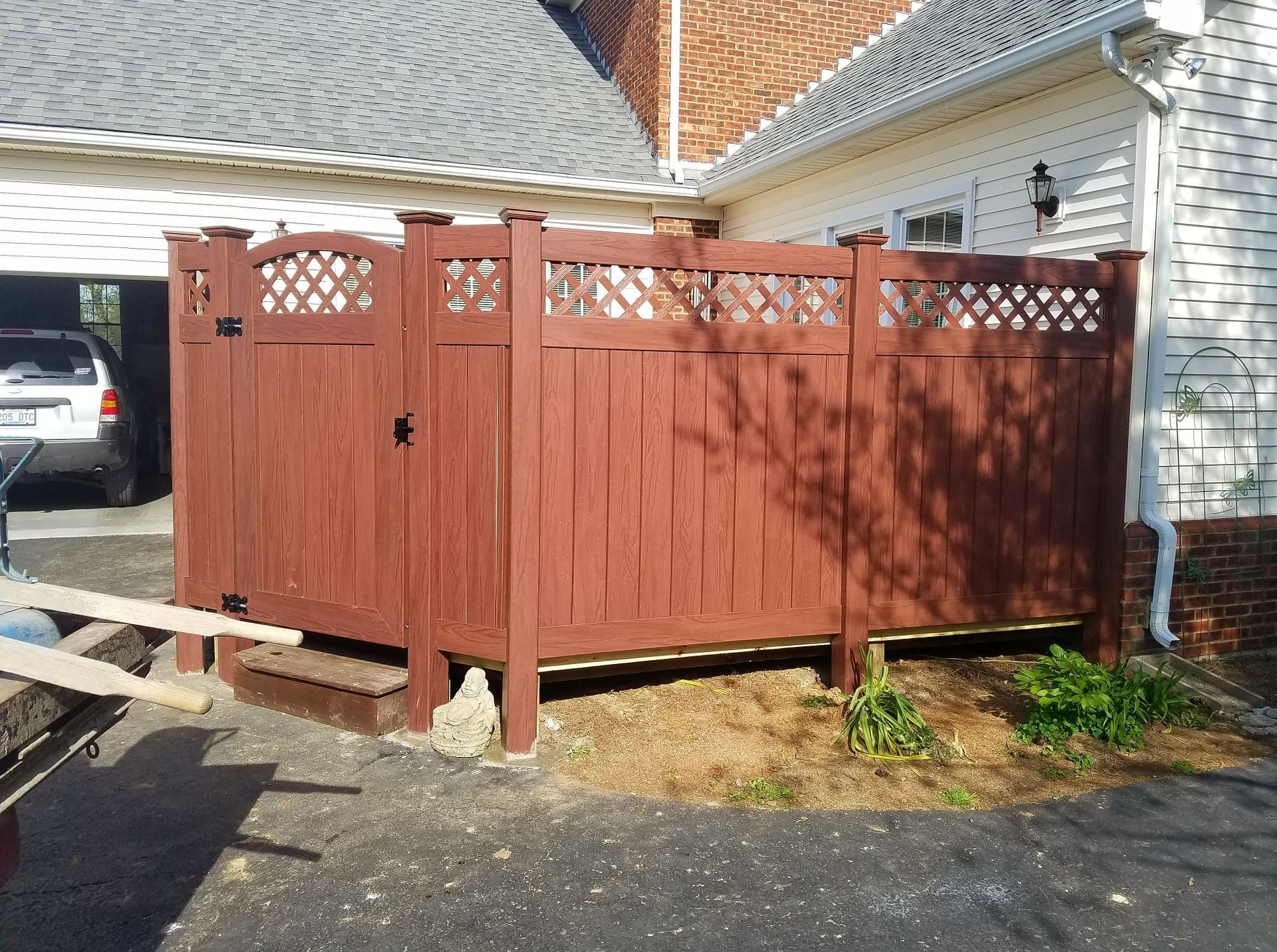 Red wooden fence and gate beside a house driveway, with lattice top panels and a parked car in the background