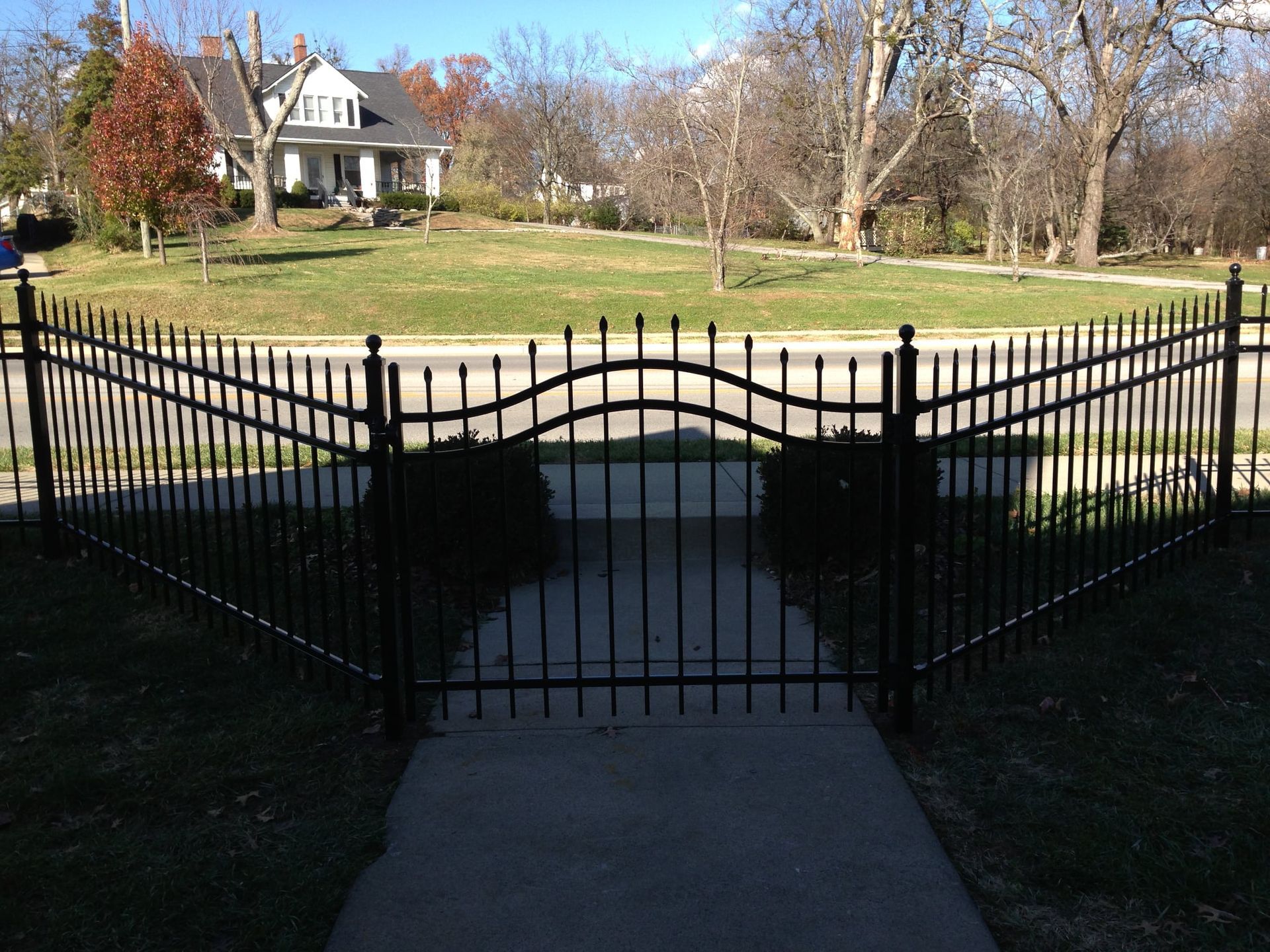 Black wrought-iron gate opening to a walkway and house with a manicured lawn beyond.