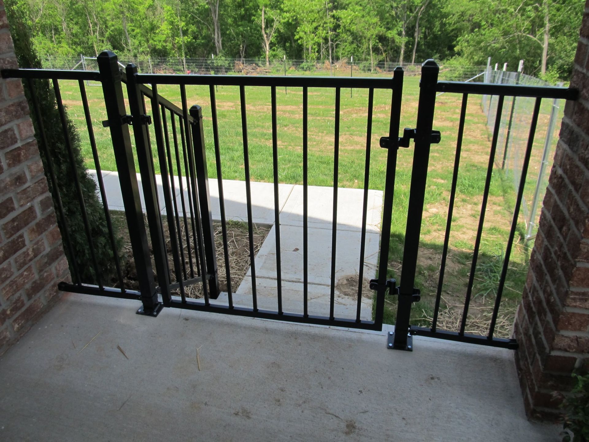 Black metal gate across a concrete porch opening, with brick pillars and a grassy yard beyond.