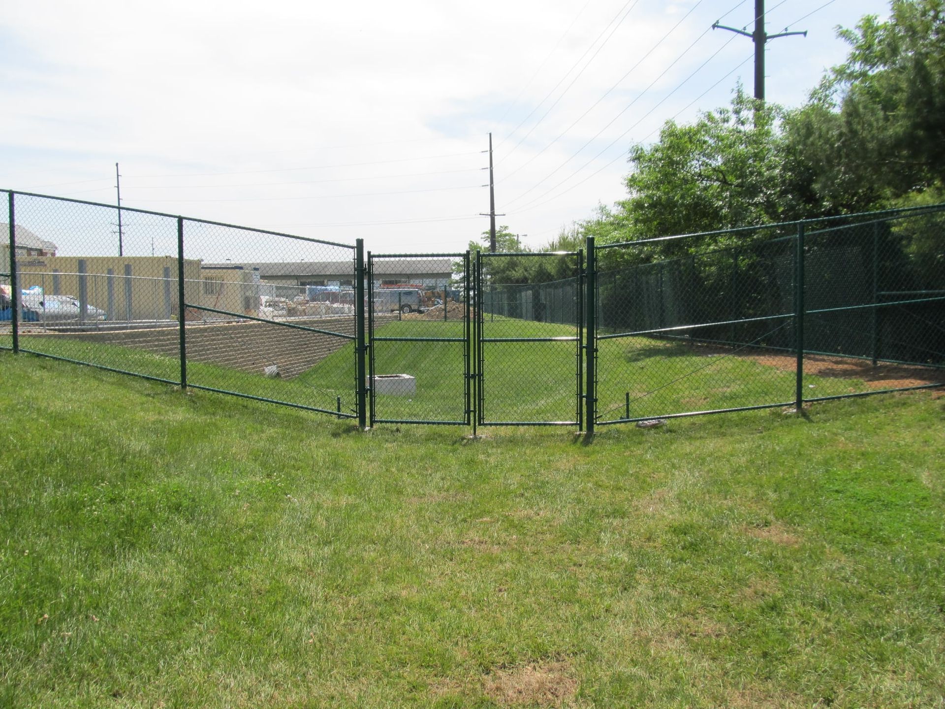 Chain-link fence enclosing a grassy field with utility poles under a cloudy sky
