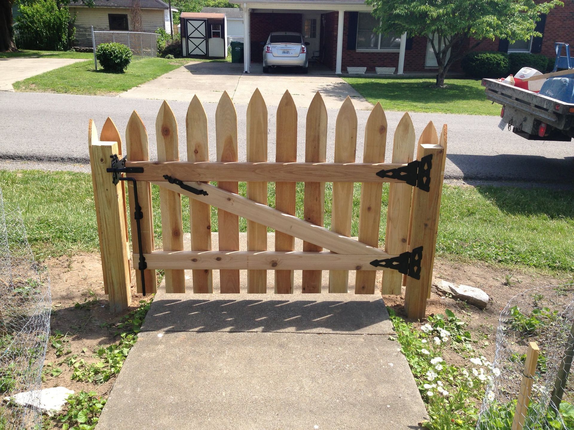 Wooden picket gate with diagonal brace blocks a concrete walkway in a front yard.
