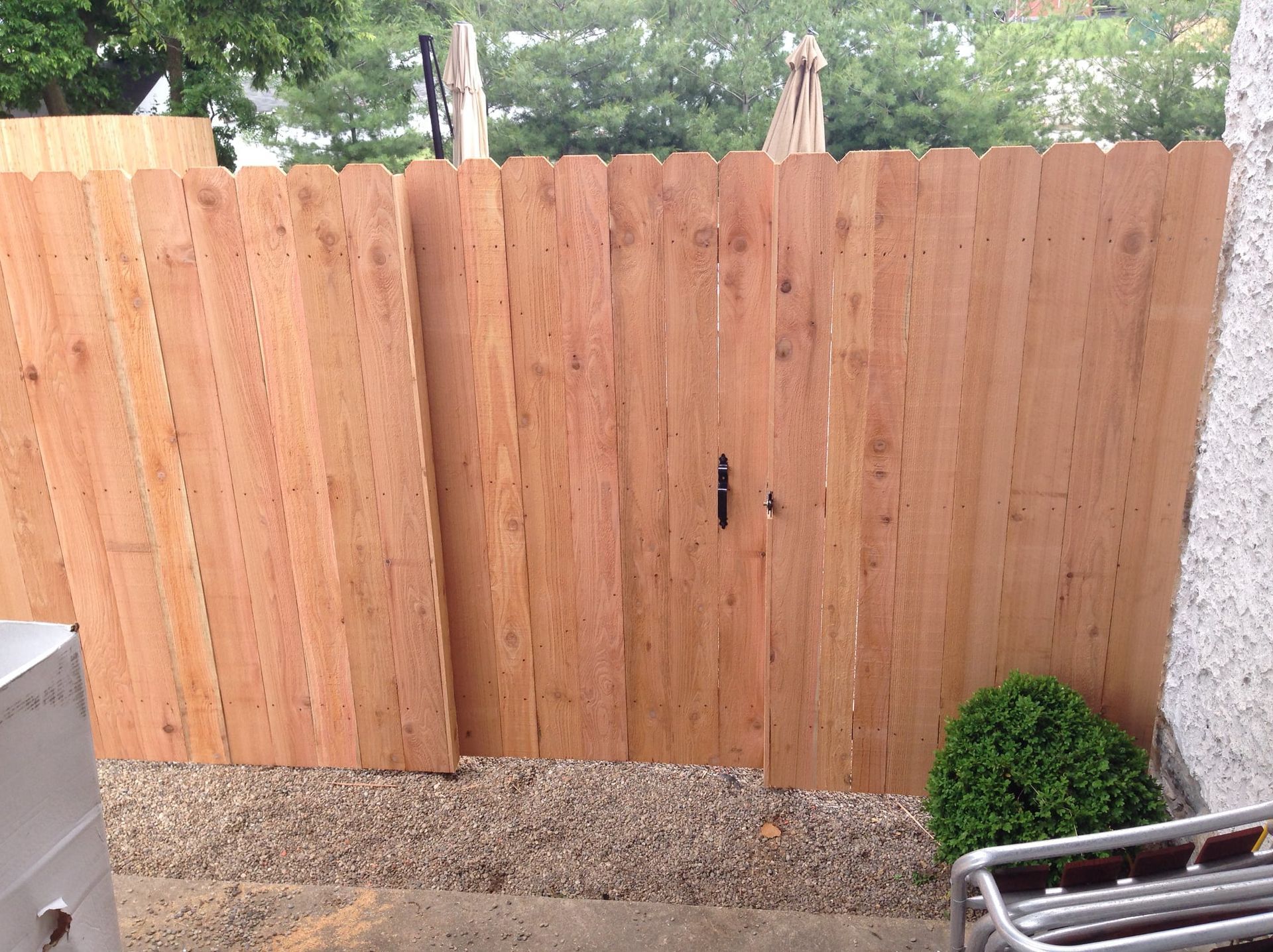 Wooden backyard fence with a gate, gravel ground, and shrubs beside a patio chair