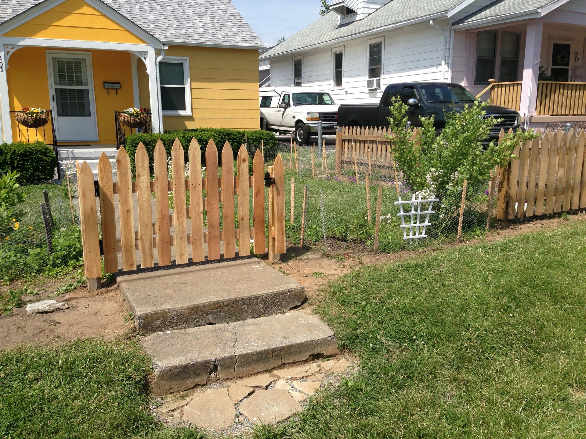 Yellow house with picket fence, front steps, and small garden in a suburban yard