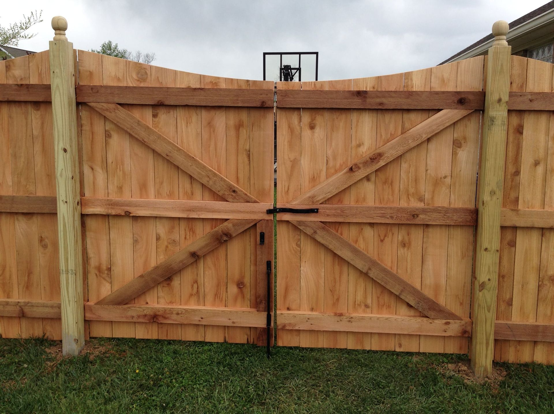 Wooden double driveway gate with diagonal braces and stone posts in a grassy yard