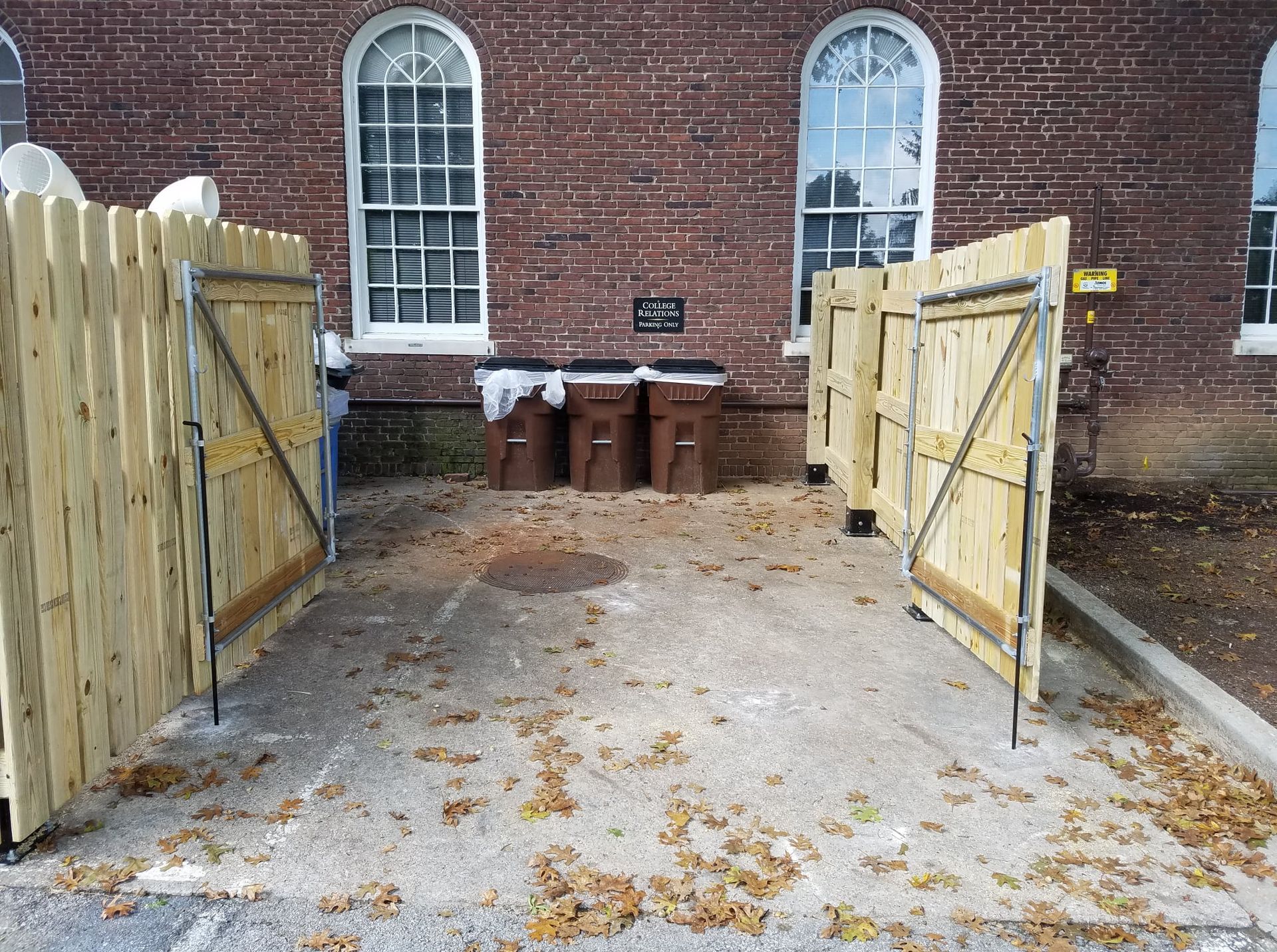 Open wooden gates in a brick courtyard with a row of trash bins against the wall