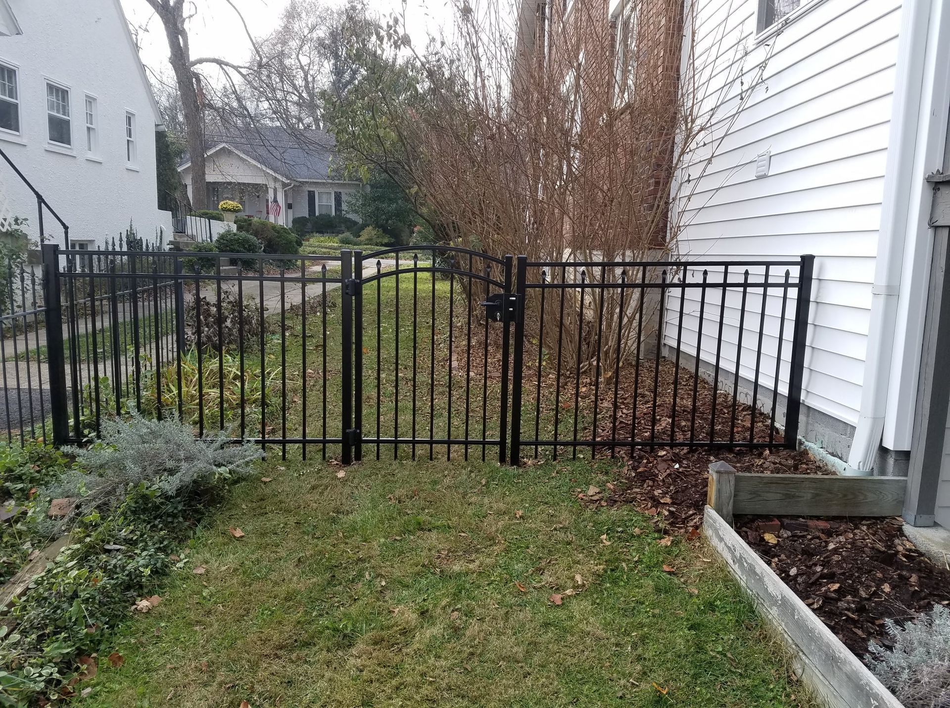 Black metal gate between two white houses, closing off a narrow grassy backyard path.