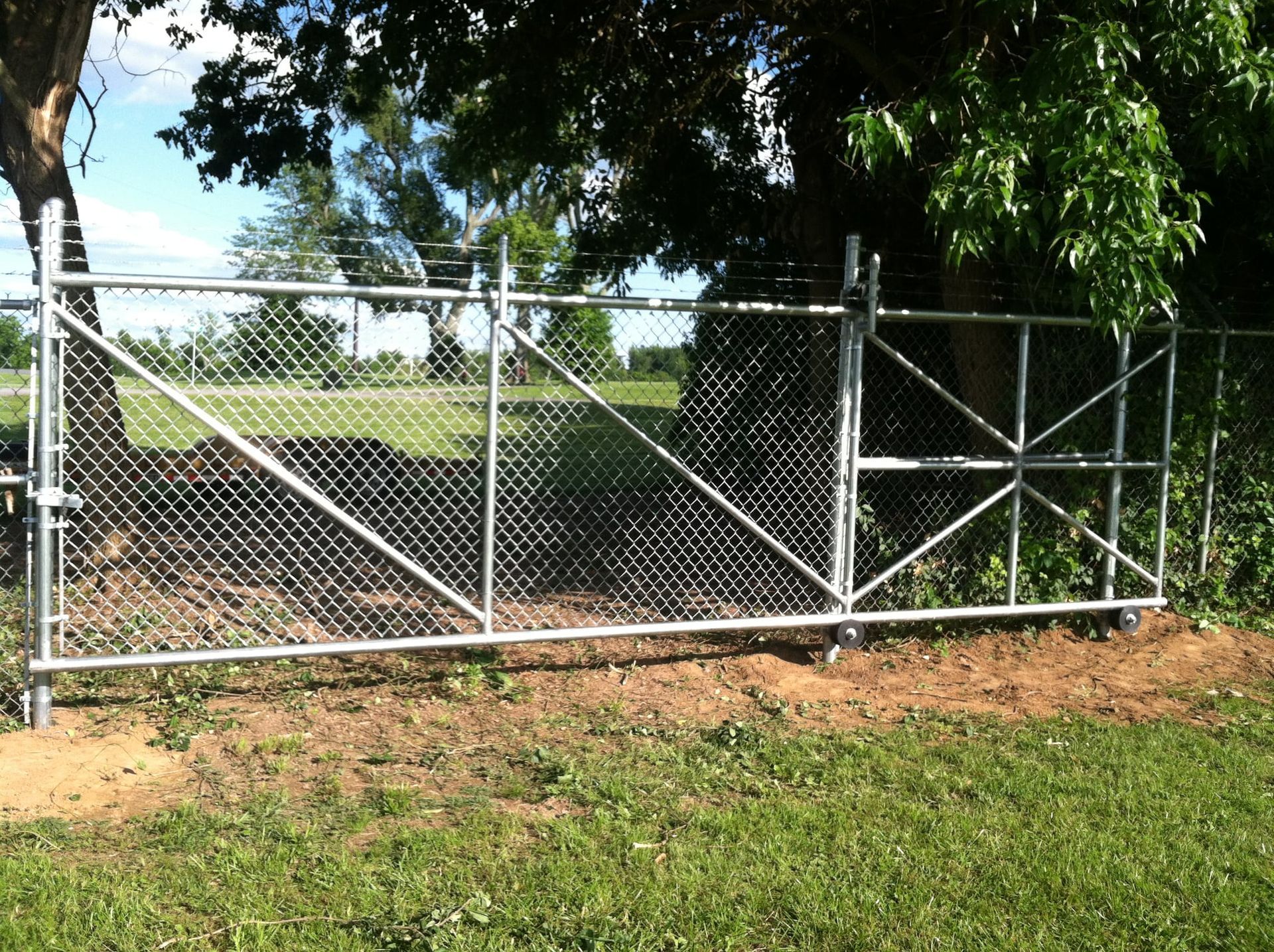 Chain-link gate beside a grassy field under large trees