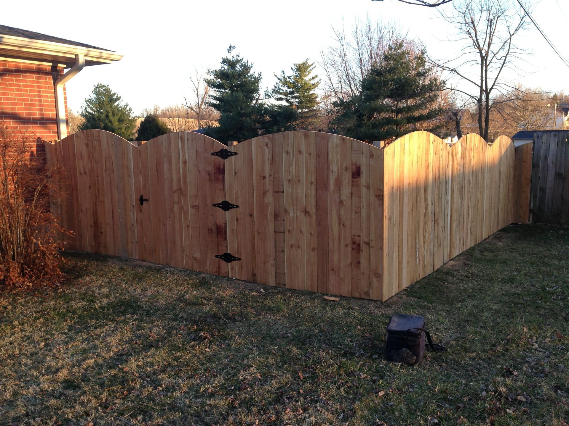 Wooden privacy fence in a backyard with sunlit panels and a brick house on the left.