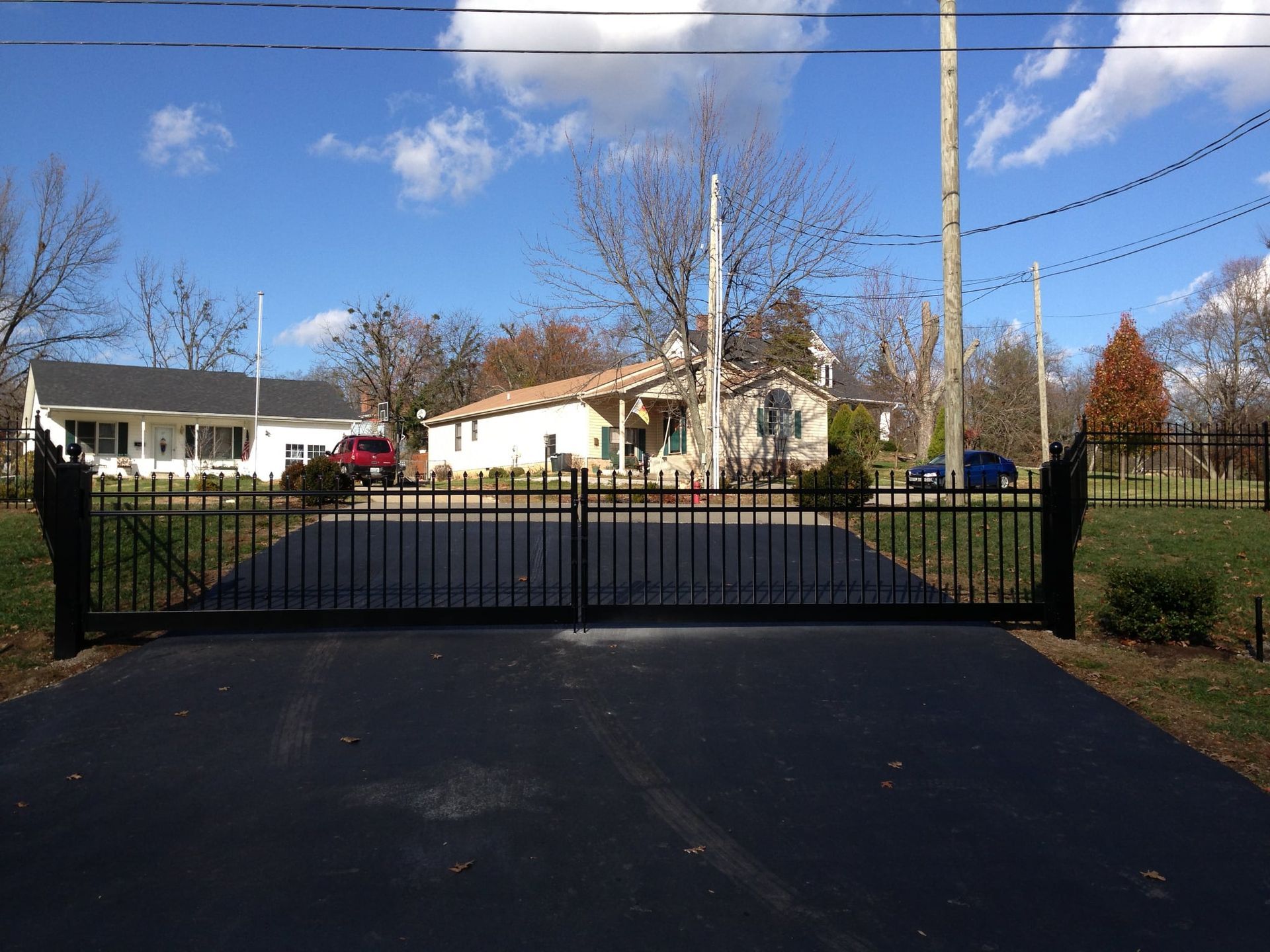 Black metal gate in front of a suburban house and driveway under a blue sky