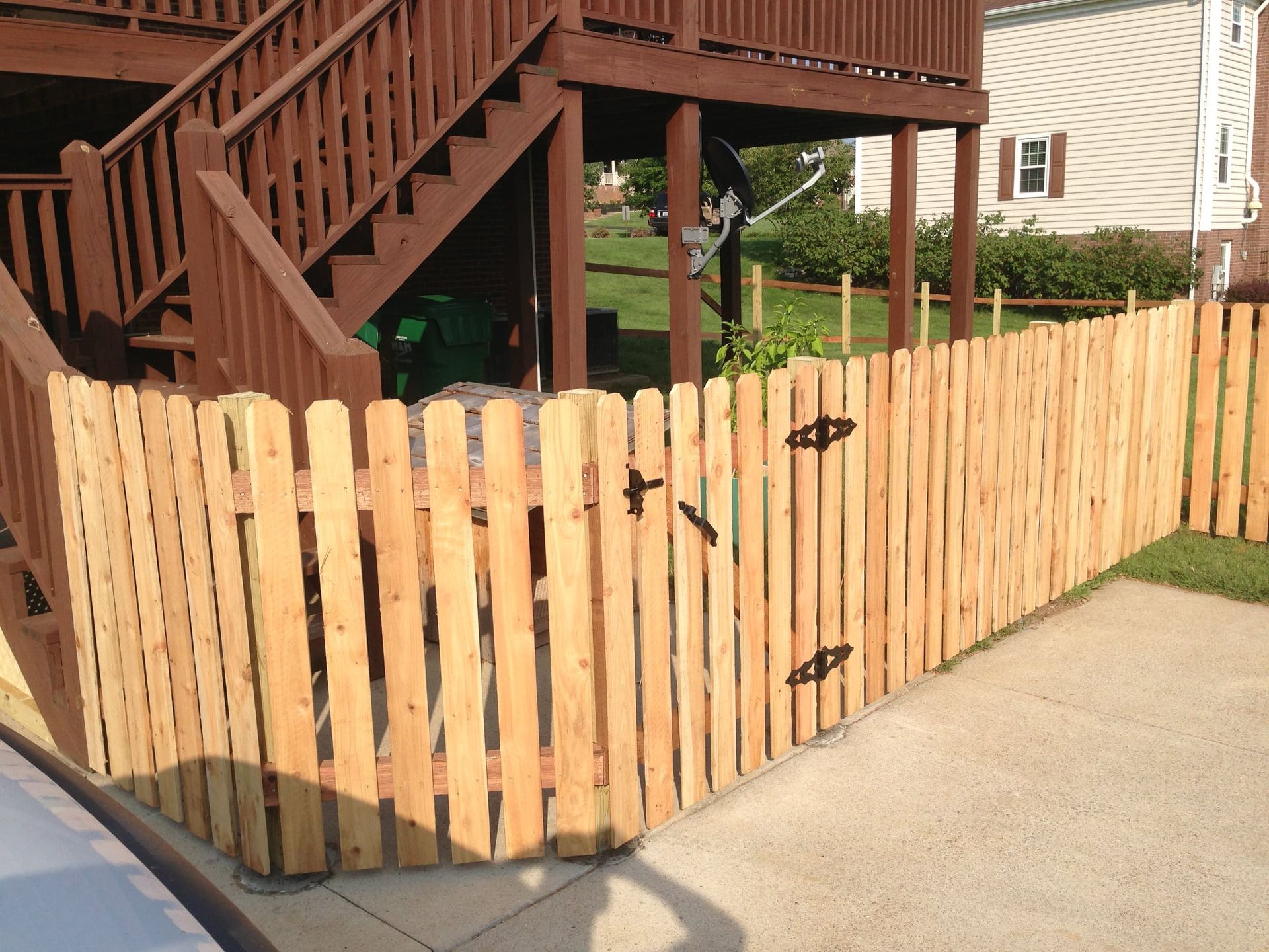 Wooden privacy fence with black hinges along a concrete driveway beside a brown house deck