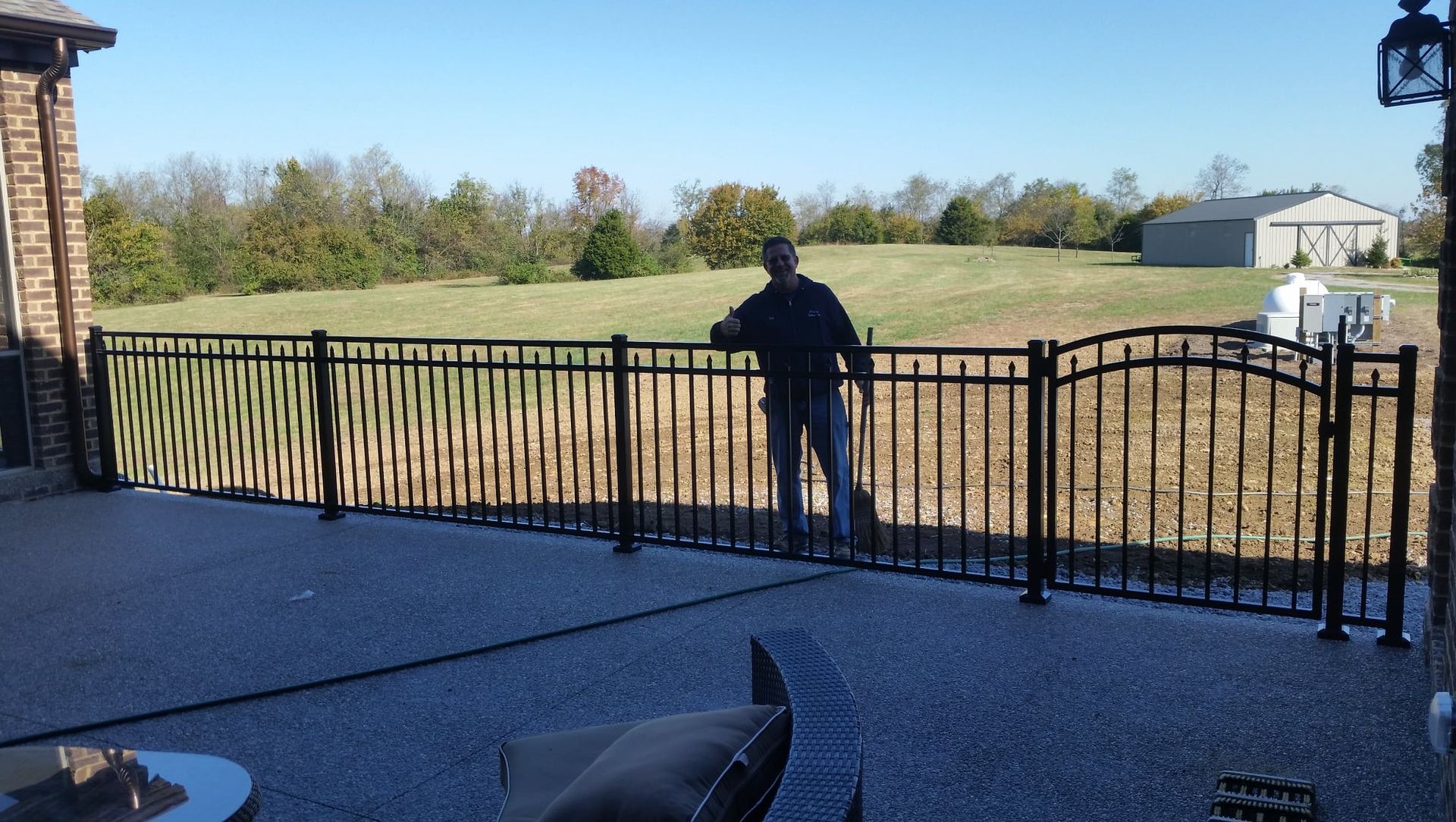 Person standing by a black fence overlooking a grassy field on a sunny day