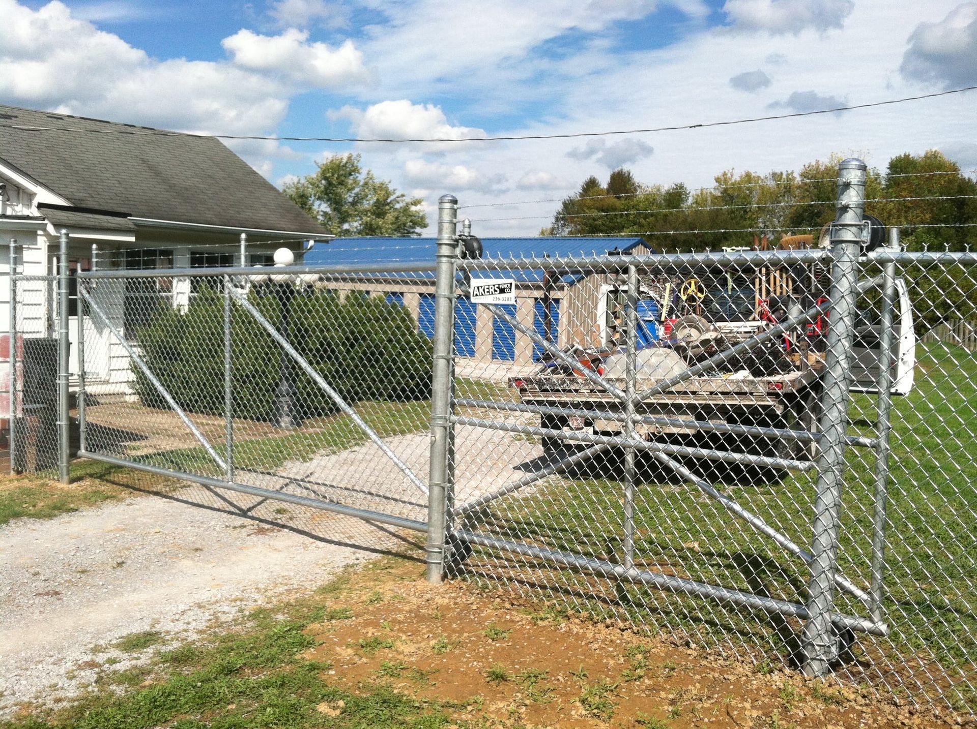 Chain-link gate in a fenced yard with a boat and blue building under a partly cloudy sky