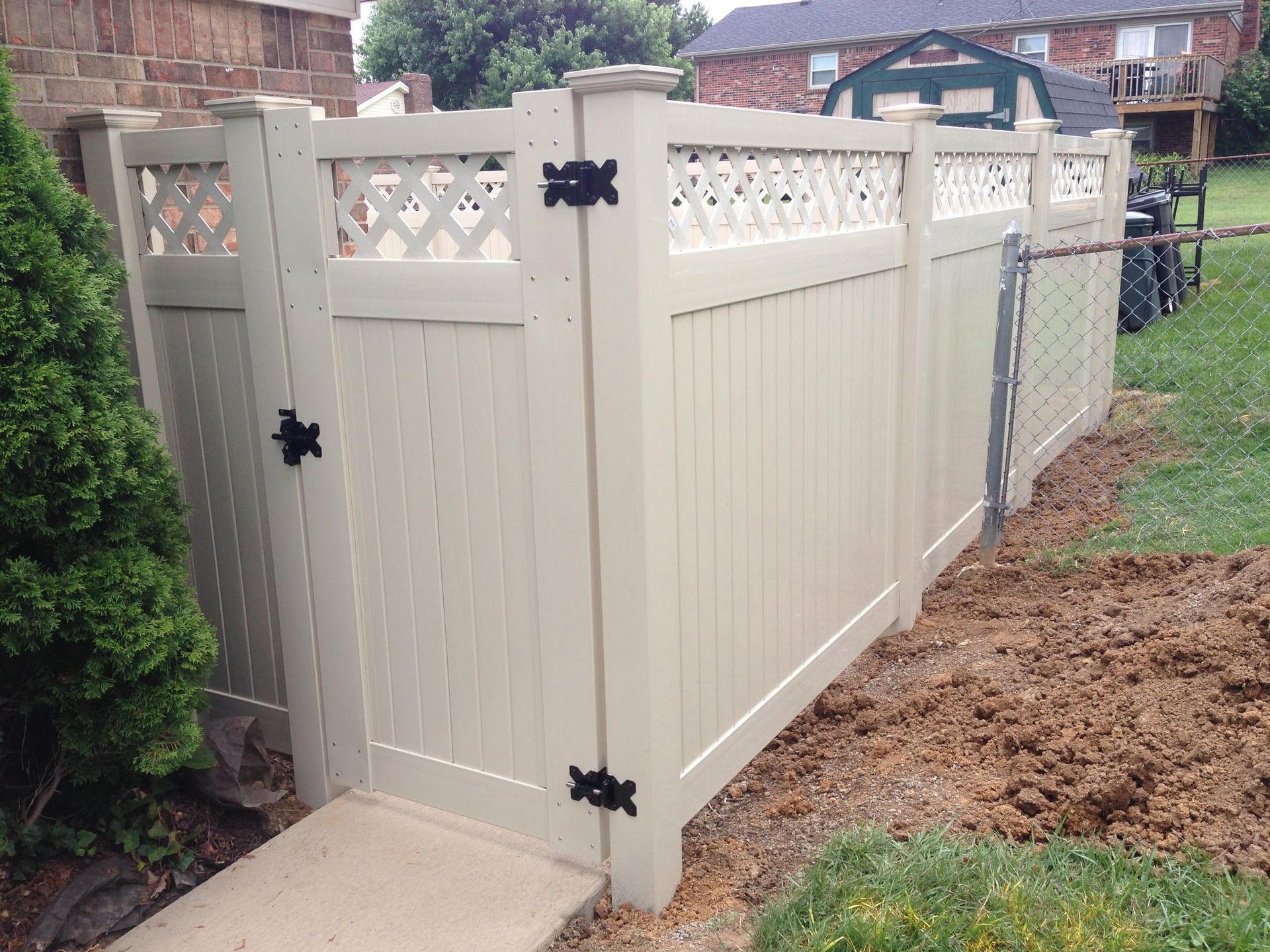 Beige vinyl privacy fence with lattice top and black hinges along a yard walkway