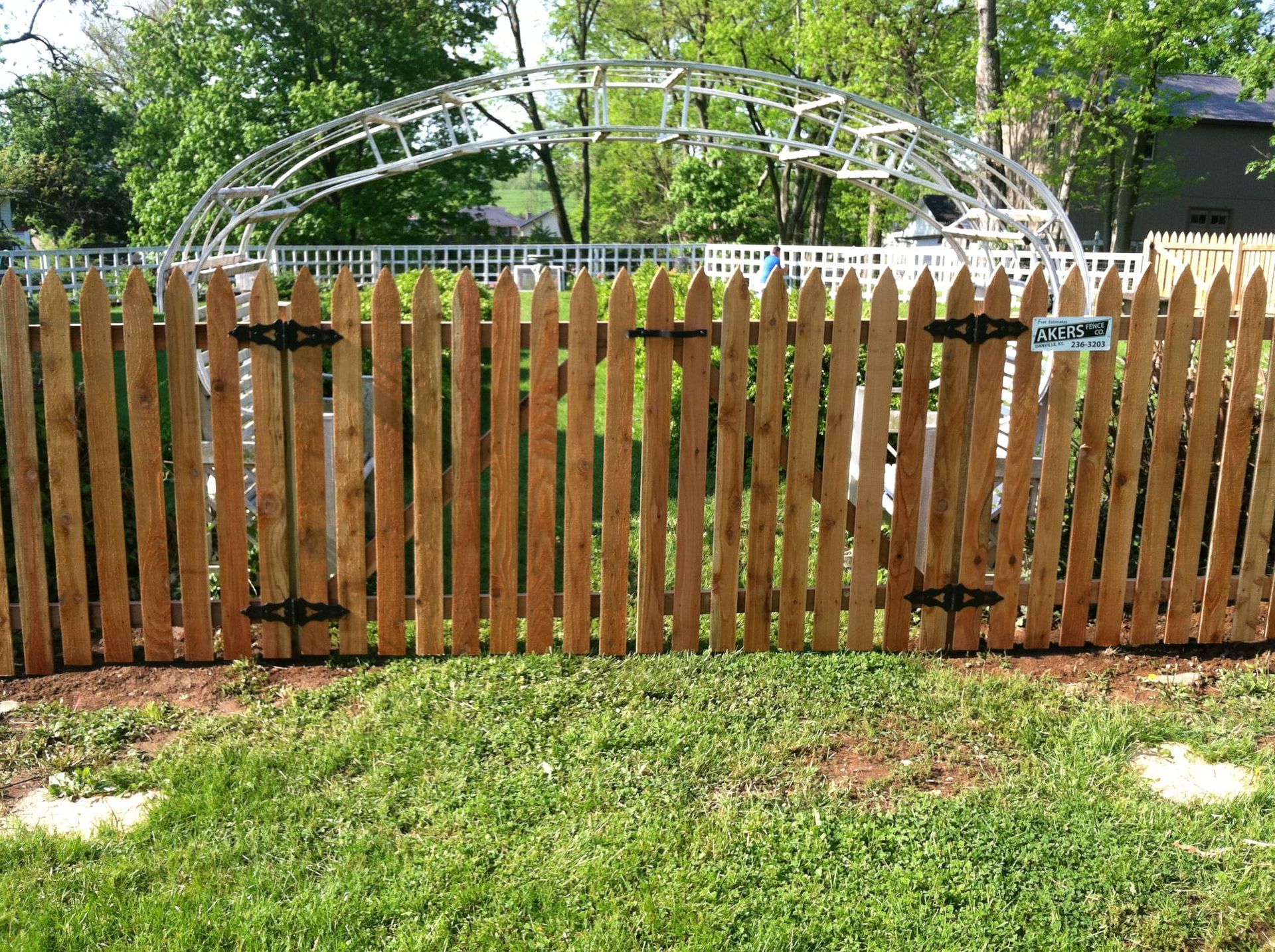 Wooden fence in front of a backyard garden arch with green grass and trees behind it