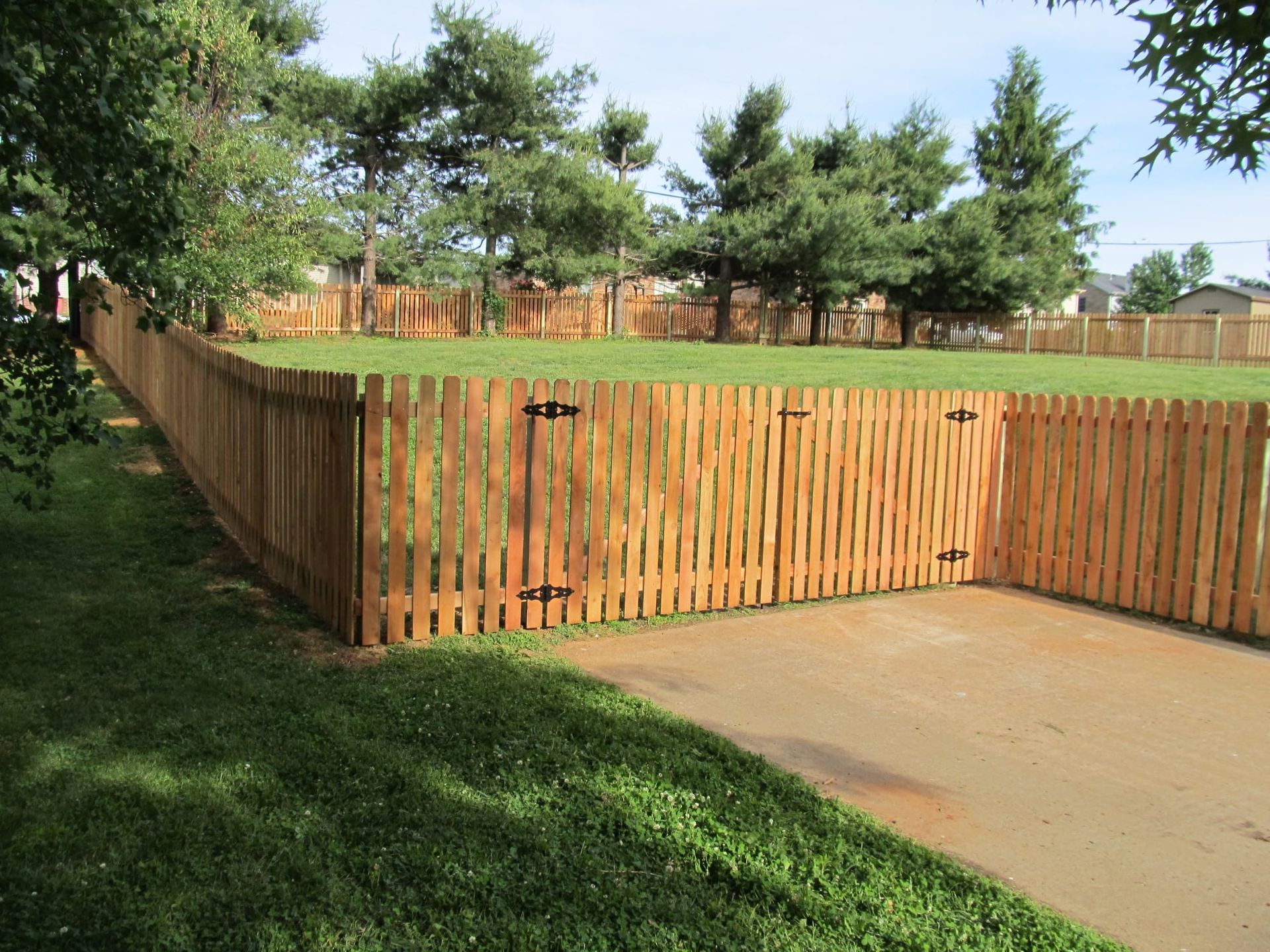 Wooden privacy fence enclosing a yard beside a concrete patio, with trees and grass in the background