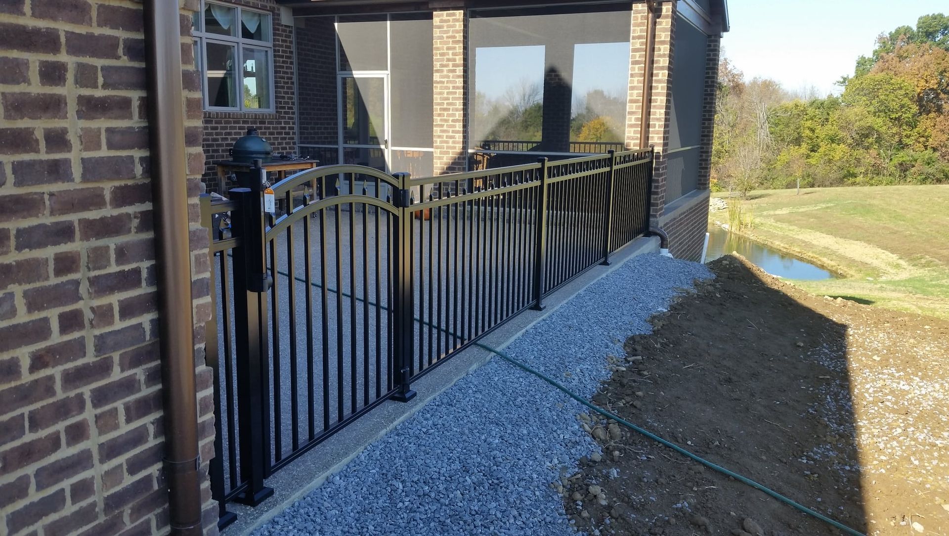 Black metal railing beside a brick house, with gravel path and porch in a sunny yard