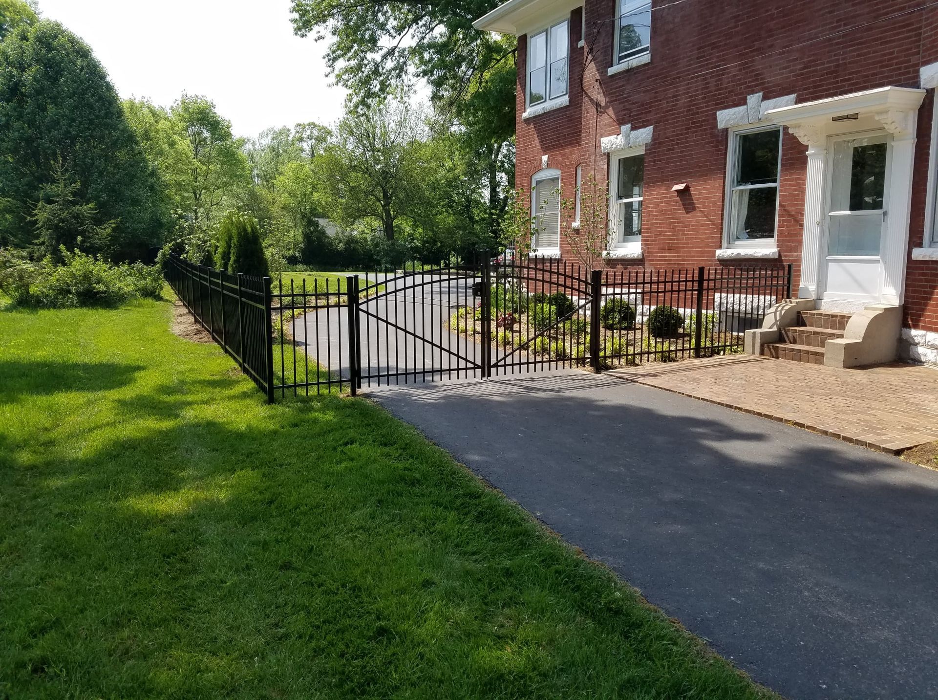 Black metal gate beside a brick house with a paved driveway and green lawn on a sunny day