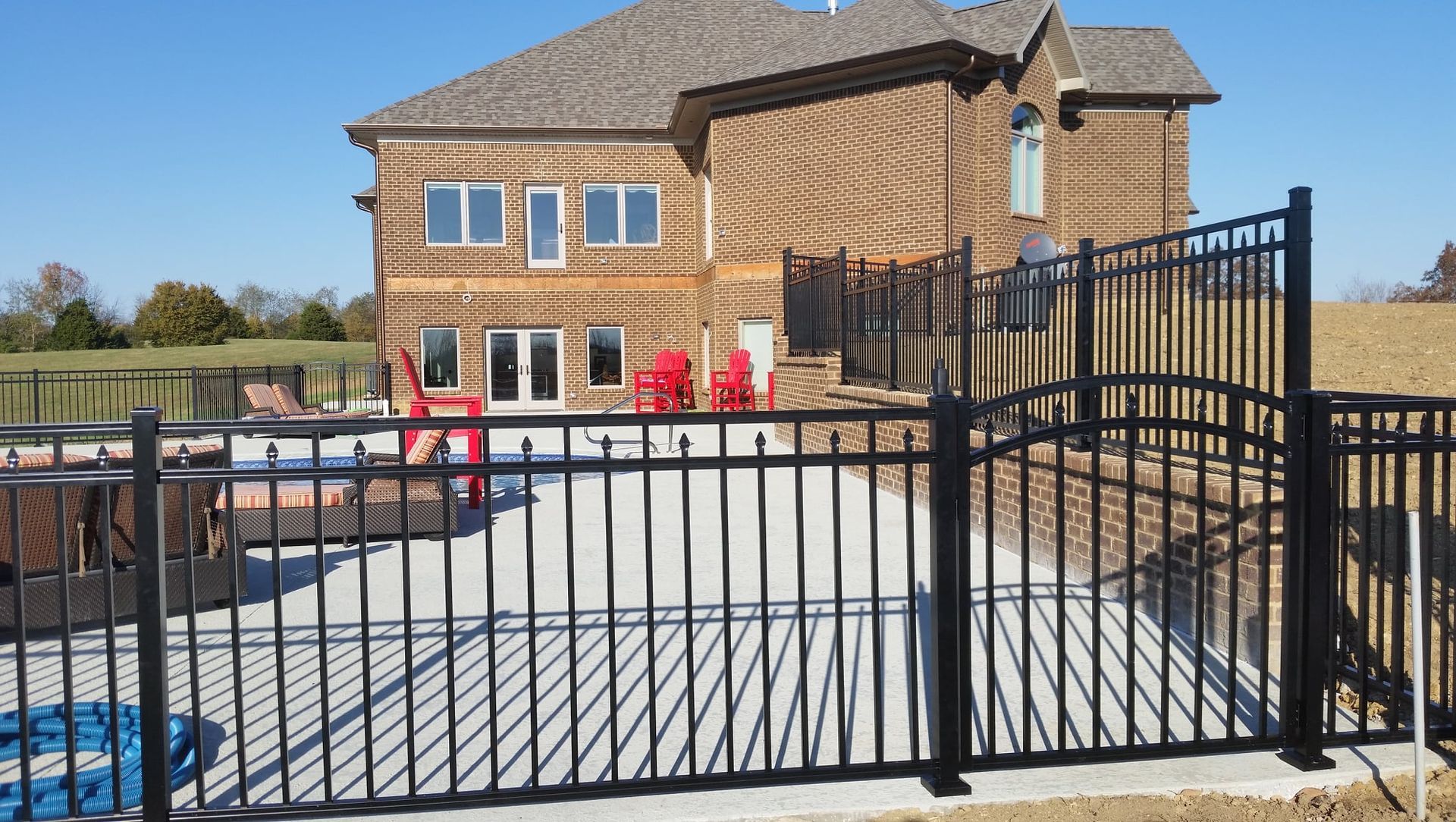 Black metal gate in front of a stone patio and two-story house on a sunny day
