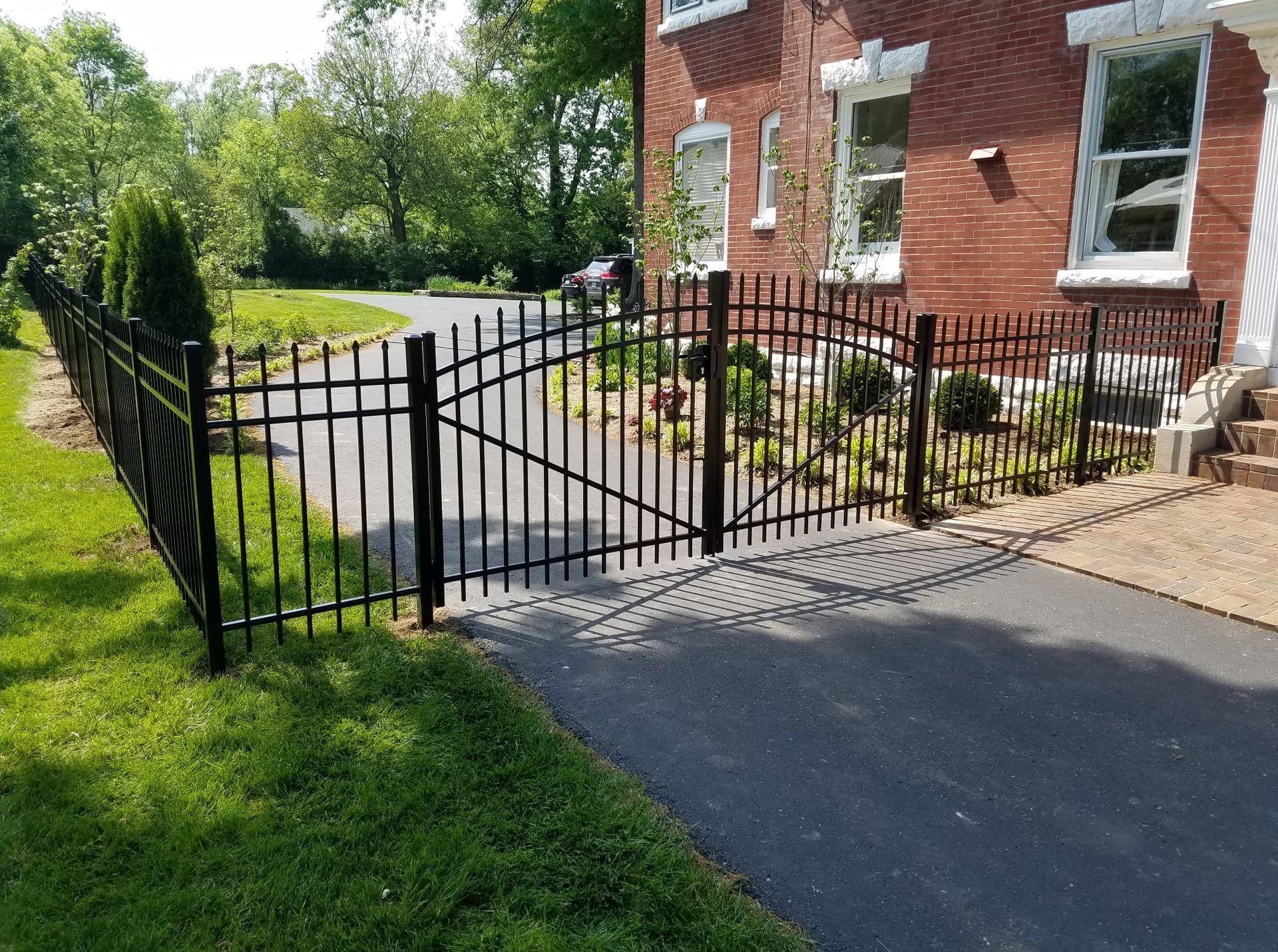 Black metal gate across a driveway beside a red brick house and green lawn.