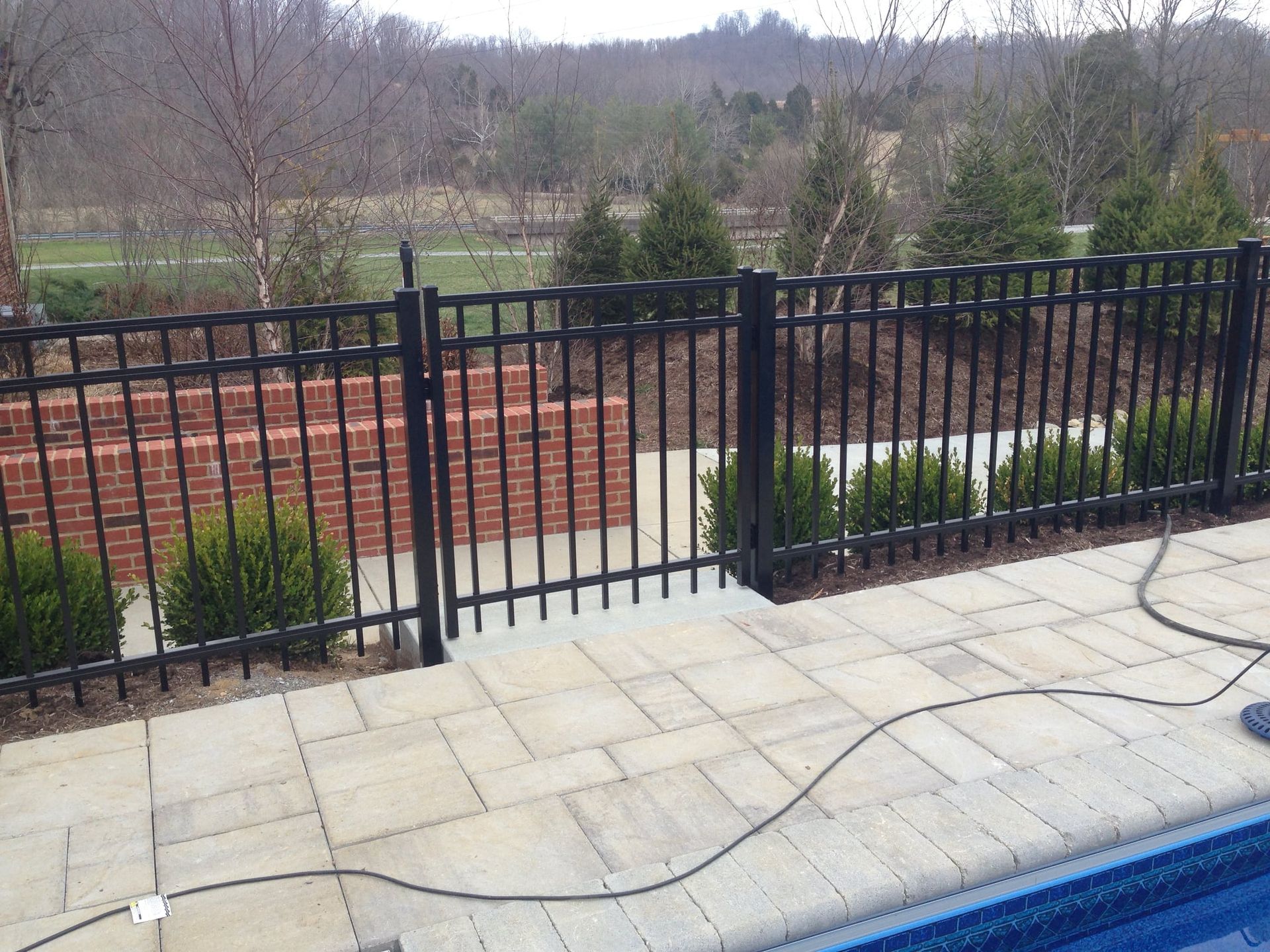 Black metal fence with gates along a patio overlooking a landscaped yard