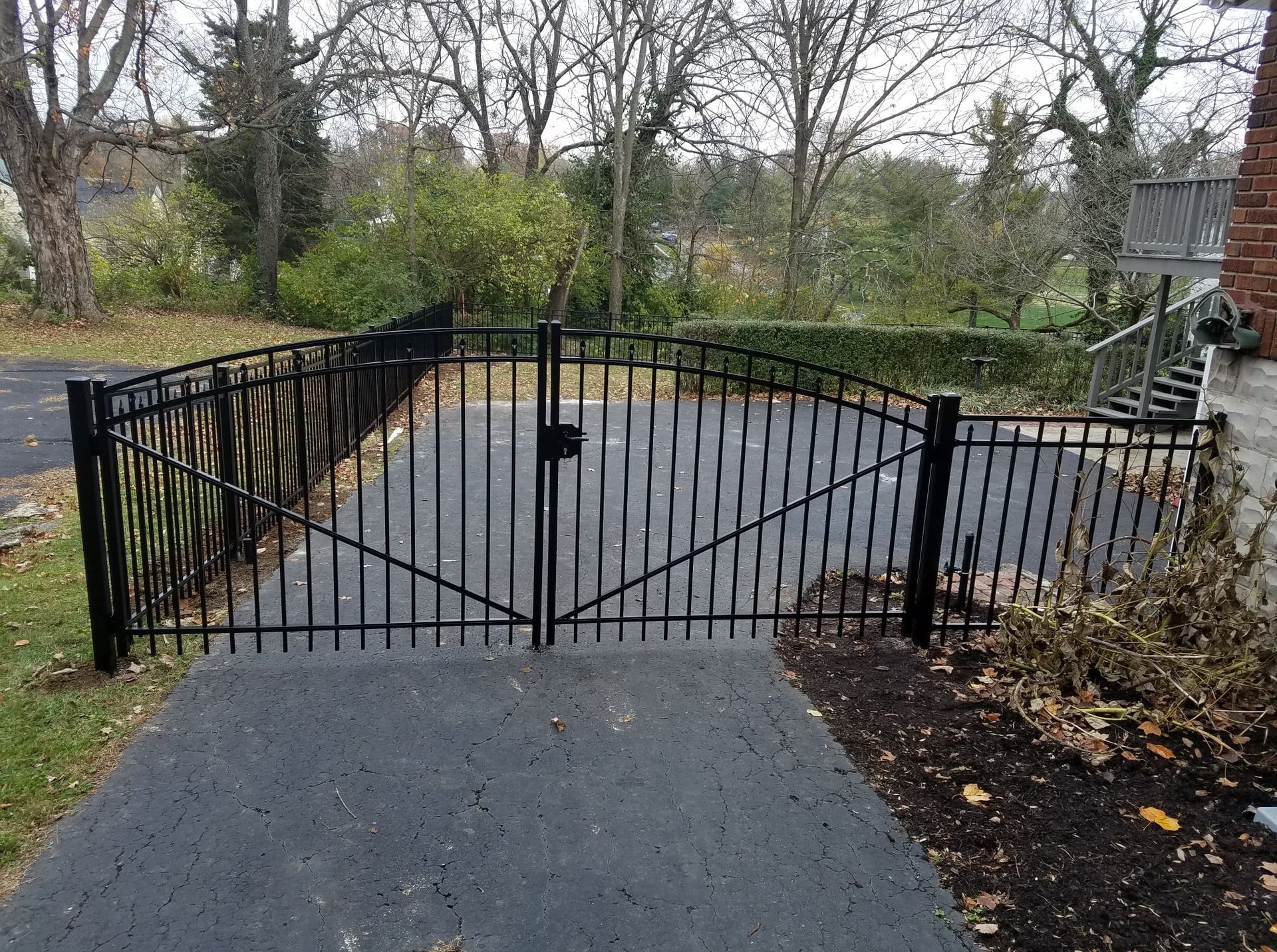 Black metal gate blocking a paved driveway in a wooded yard