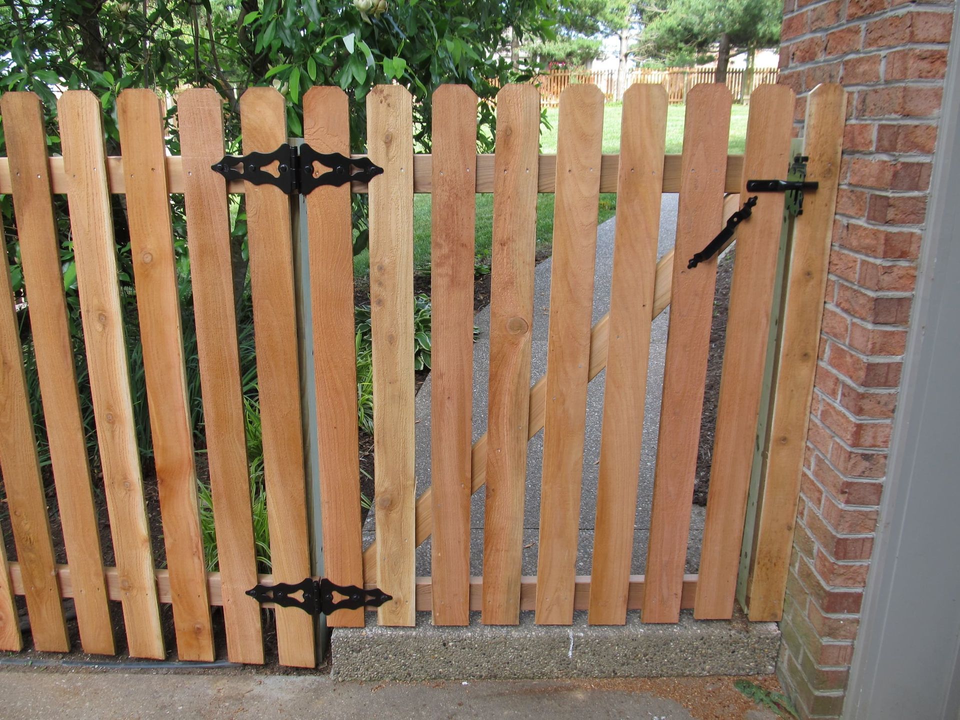Wooden garden gate with black hinges beside a brick wall and grassy yard