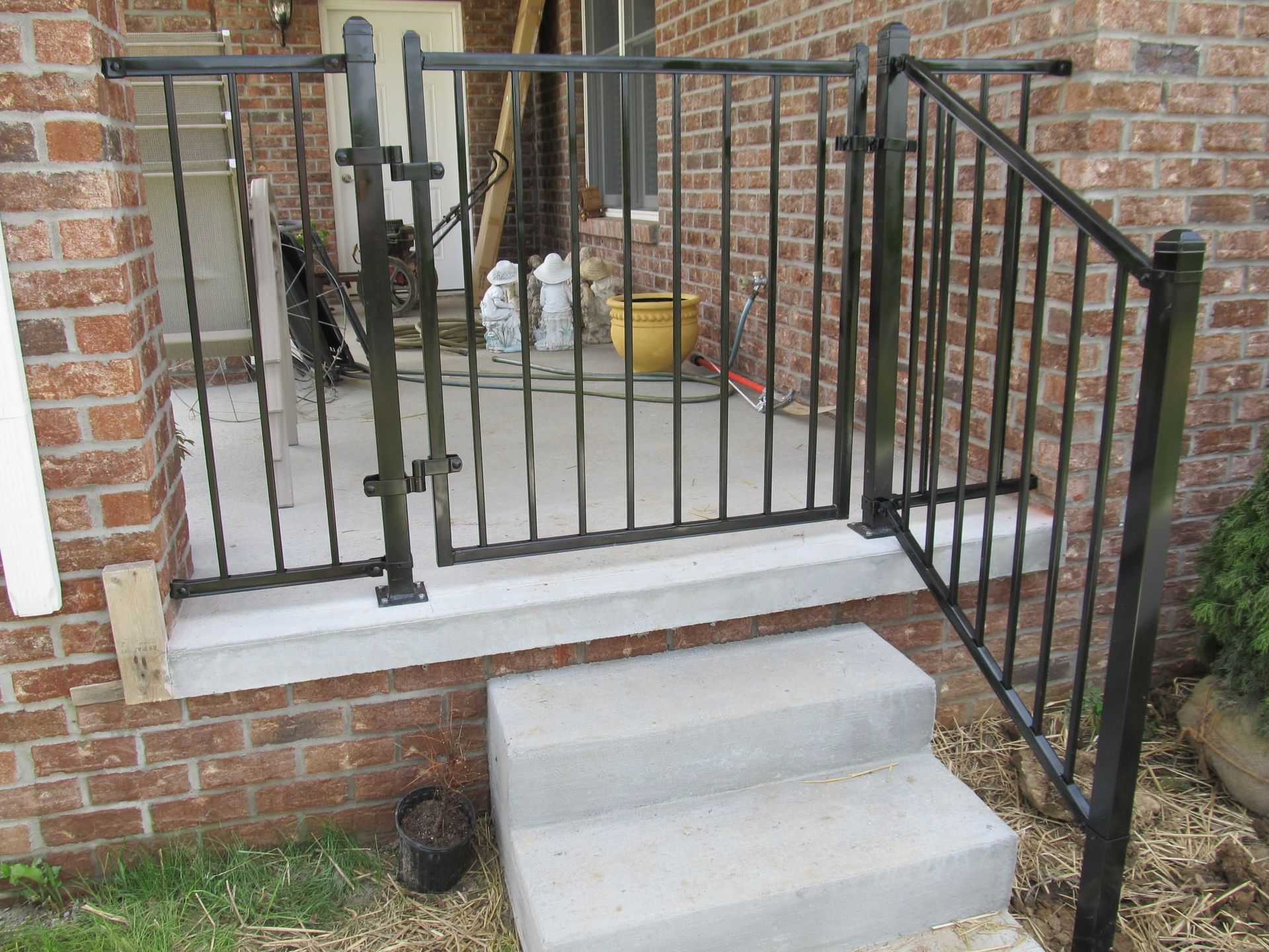 Front porch with concrete steps and black metal railing on a brick house.