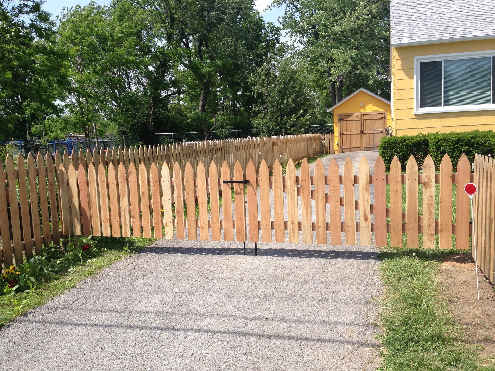 Wooden driveway gate across a gravel driveway beside a yellow house and fenced yard
