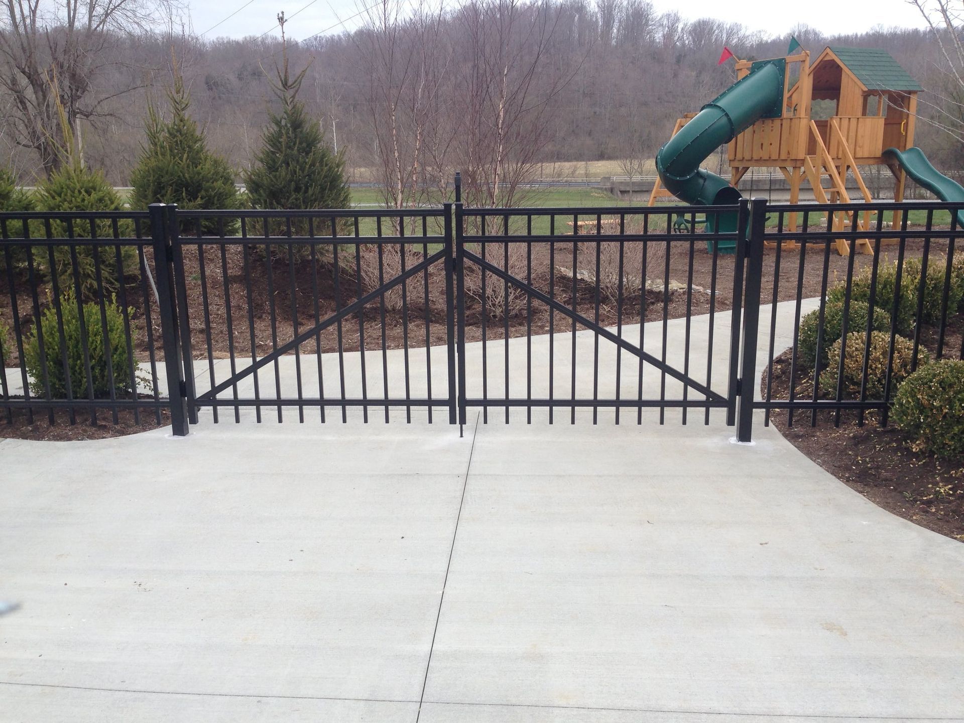 Black metal gate blocking a playground with a green slide beyond a concrete path