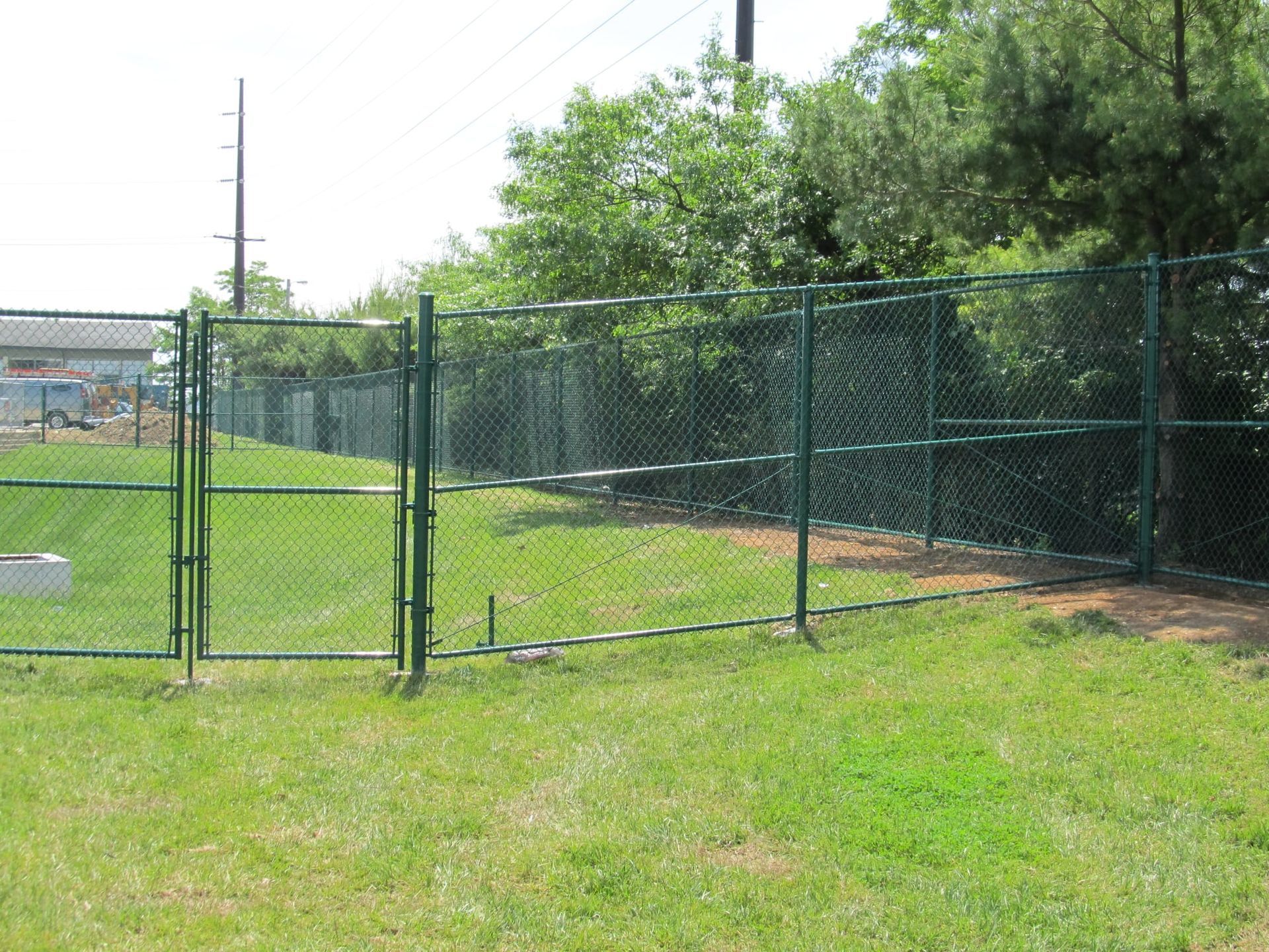 Chain-link fence along a grassy field with trees and utility poles in the background.