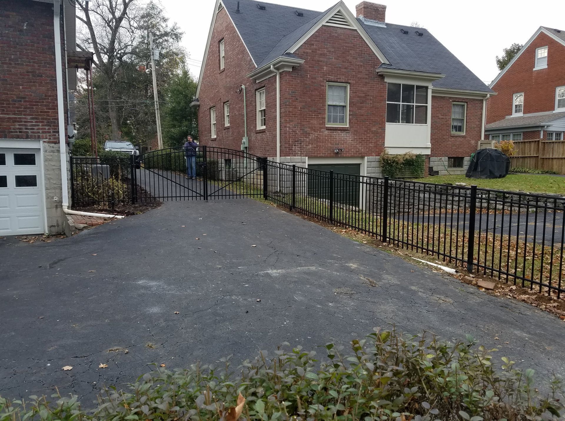Brick house and paved driveway beside black metal fence on an overcast day