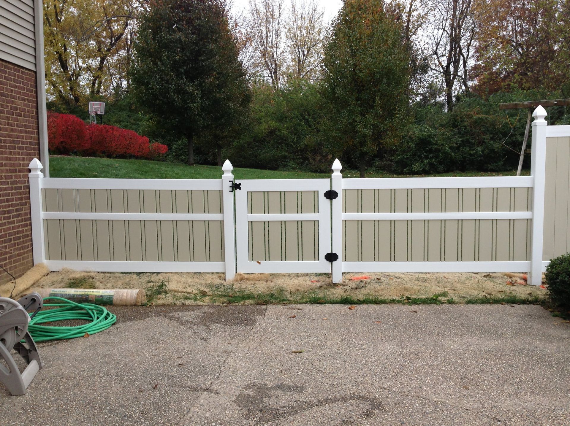 White wooden driveway gate with fence in front of shrubs and trees