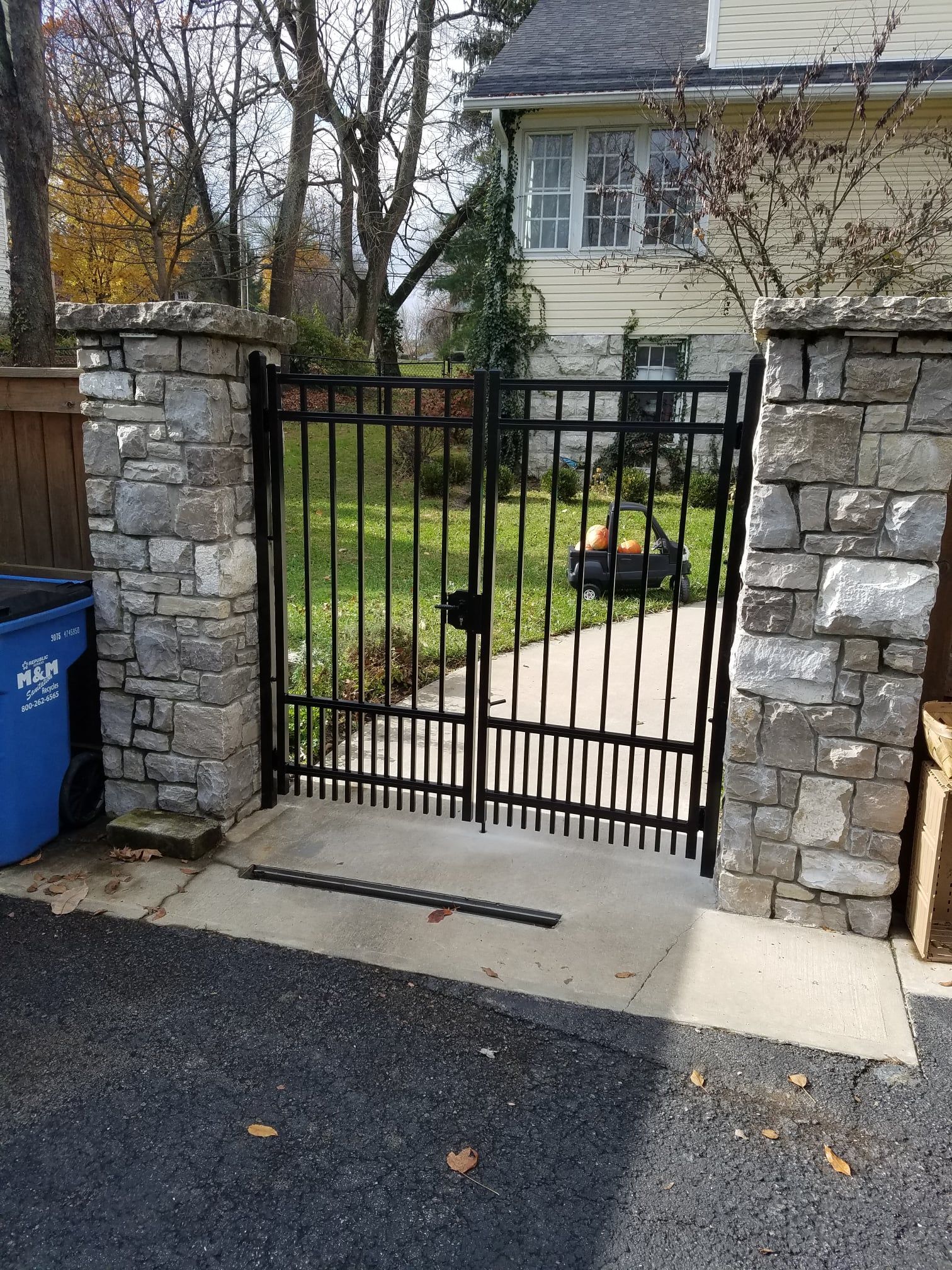 Black metal gate between stone pillars leading to a front yard and house walkway