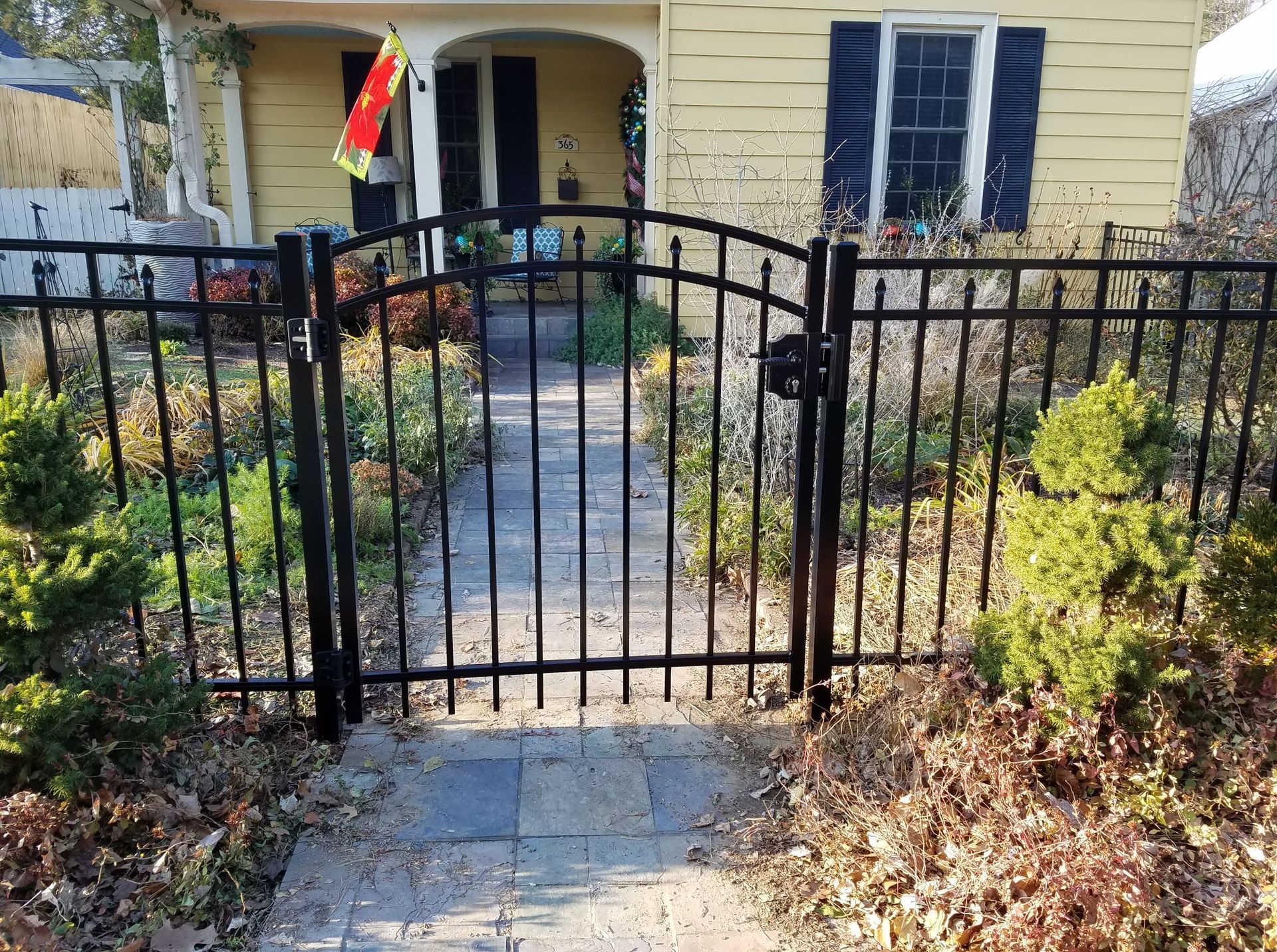 Black metal gate and walkway leading to a yellow house with blue shutters and a porch.