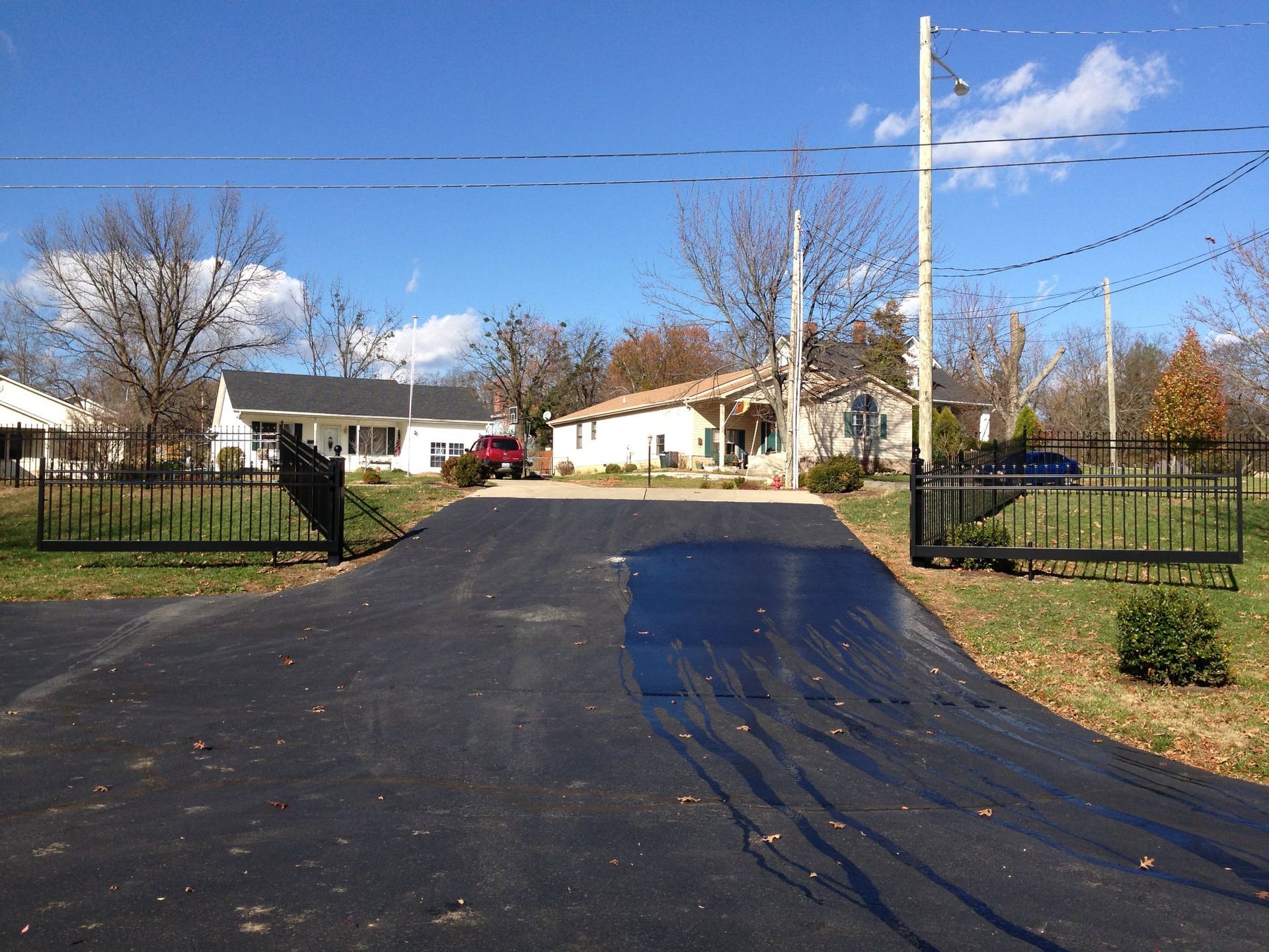 Driveway entrance with open black gates leading to a suburban home on a sunny day.