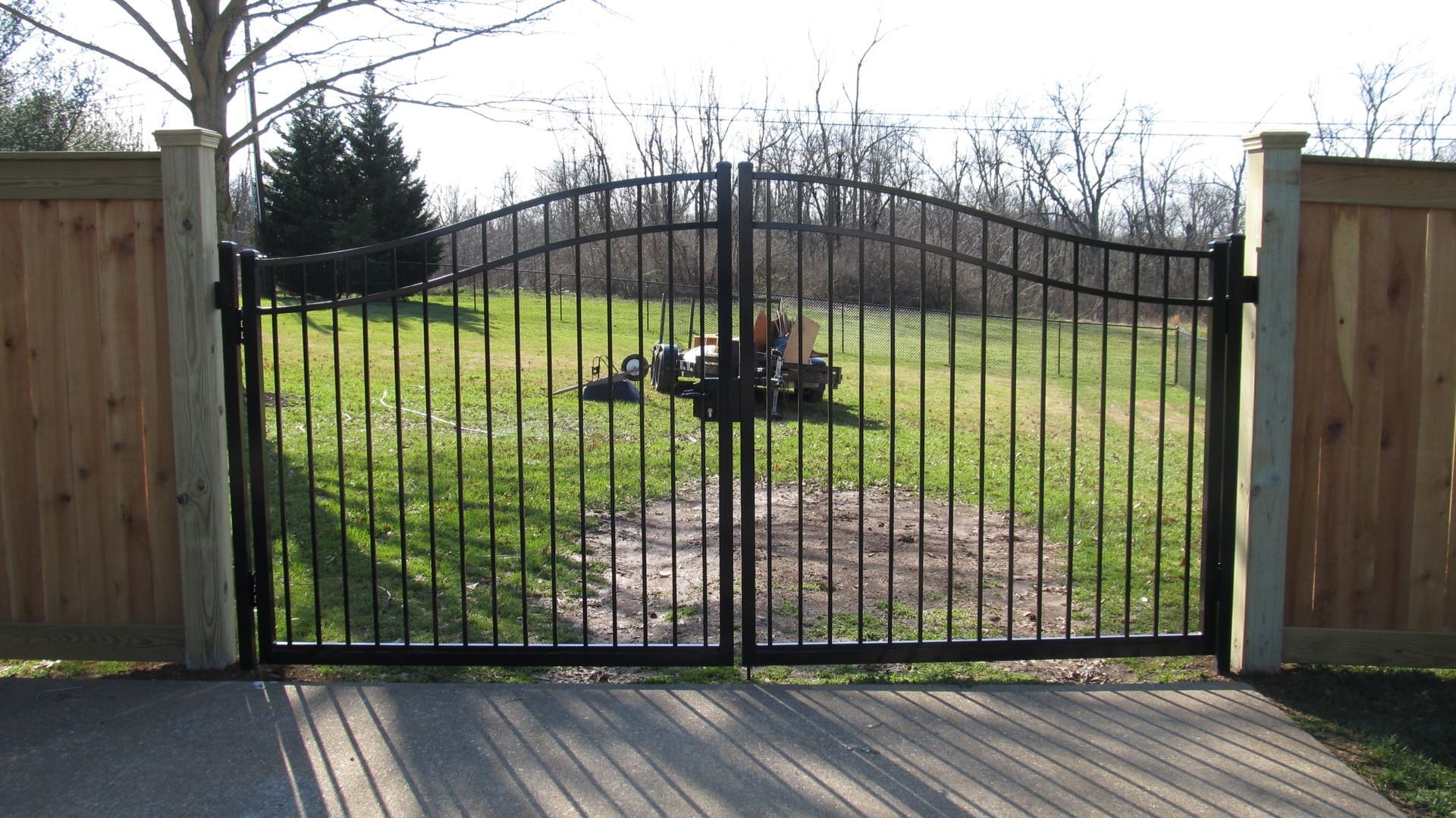 Black metal gate opening to a grassy yard with a tree stump and wooden fence posts on either side.
