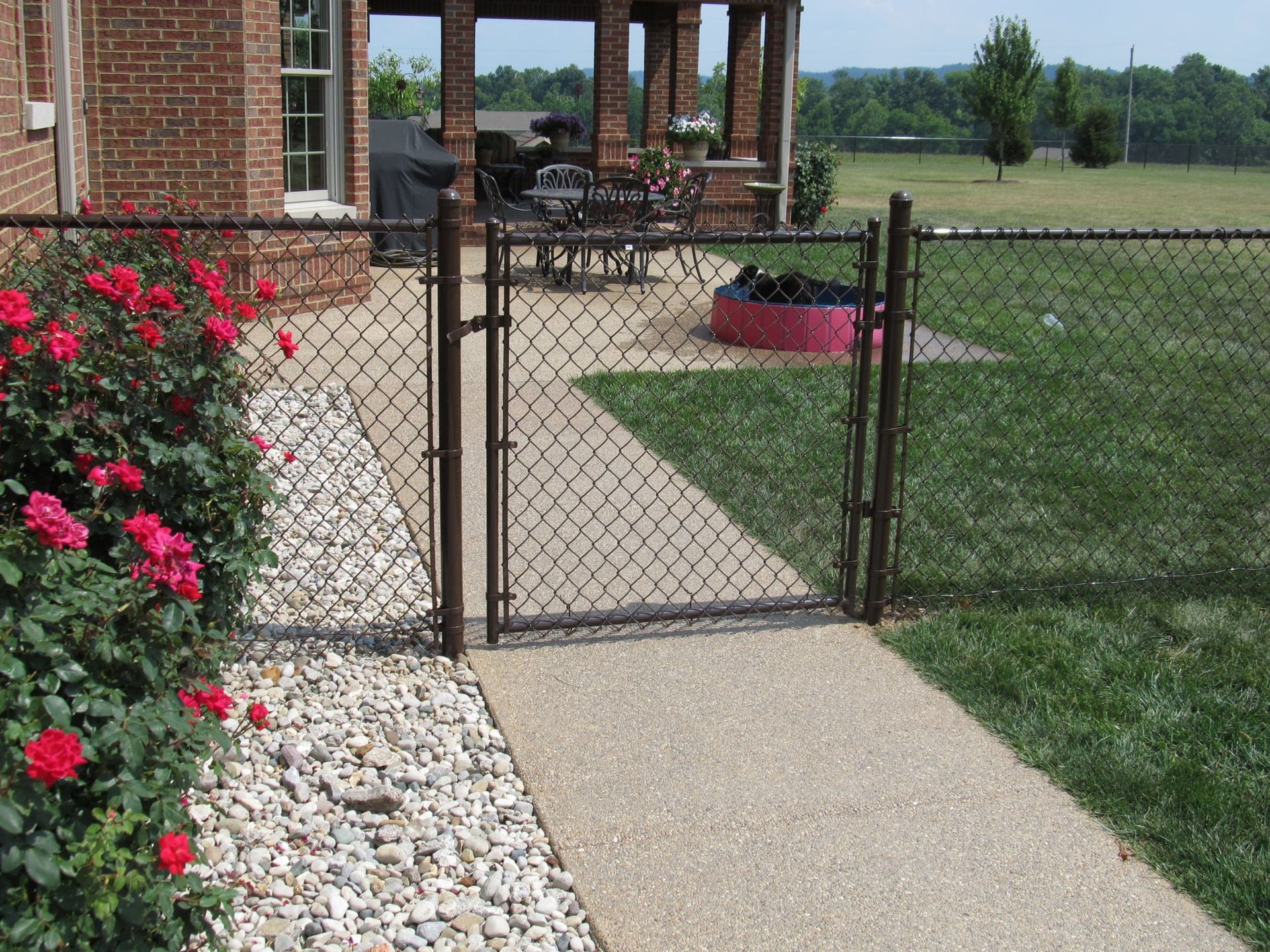 Brick house patio with open black gate, flower bed, and walkway beside a grassy yard