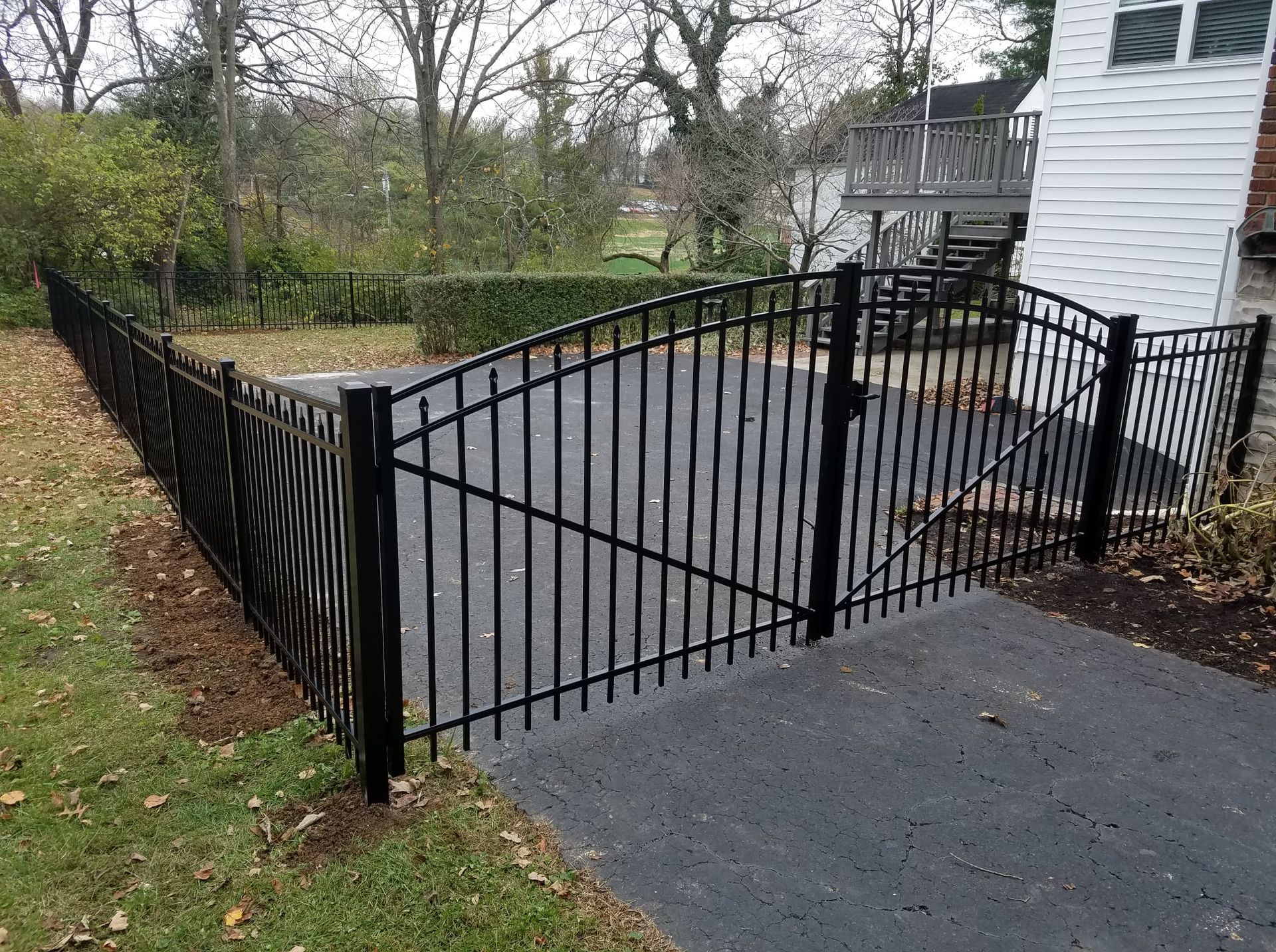 Black metal gate and fence beside a house driveway in a wooded yard