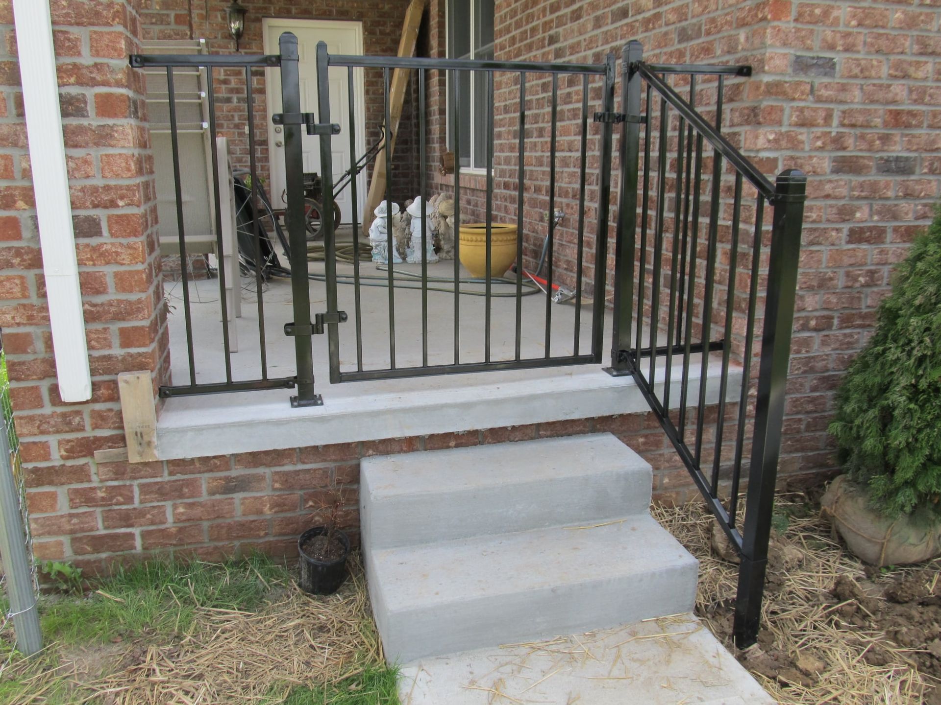 Small concrete porch steps beside a black metal railing and brick house wall.