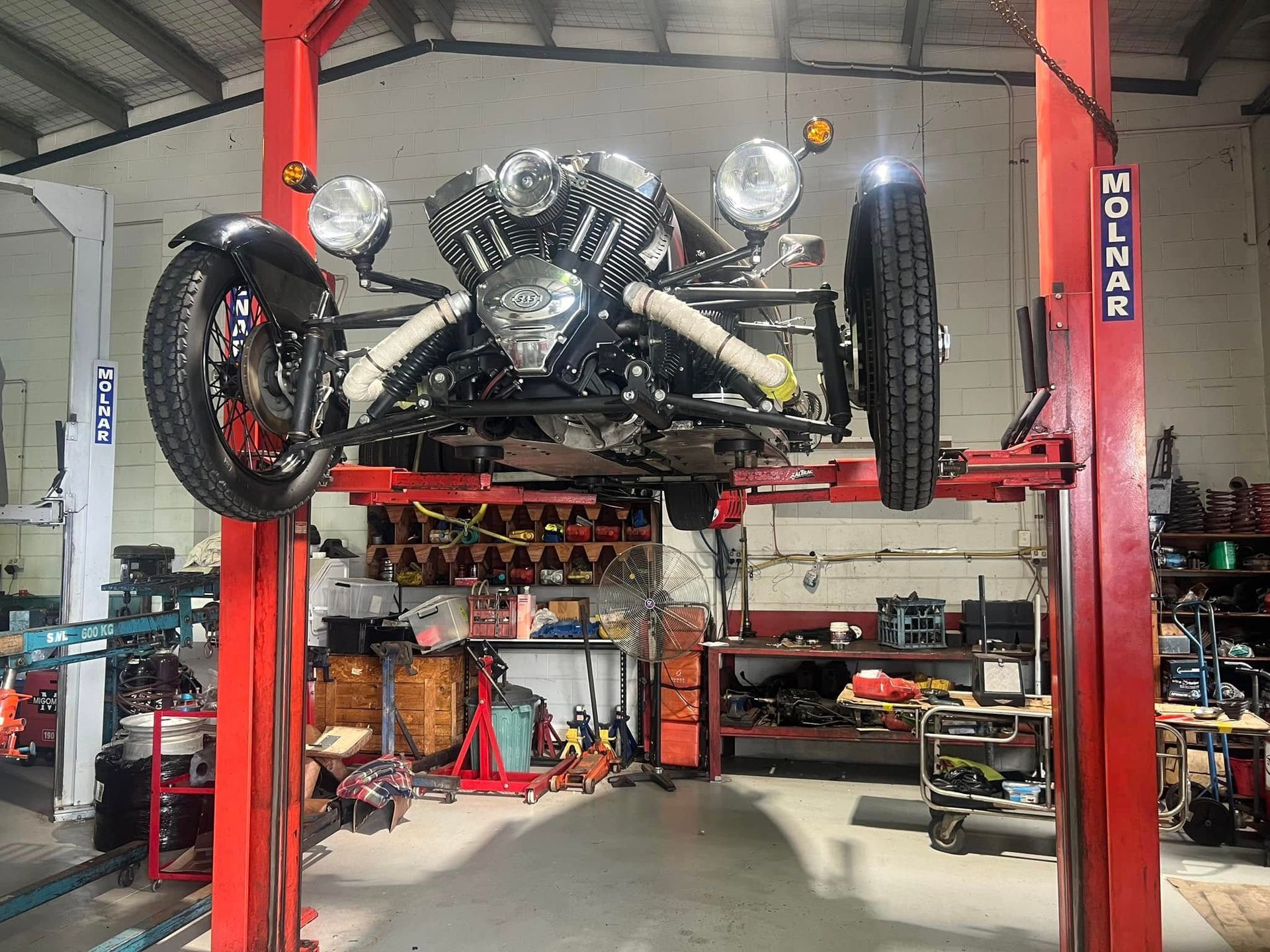 A Three-wheeled Vehicle Is Hoisted On A Red Hydraulic Lift — Auto Inspections & Road Services N.T. in Woolner, NT