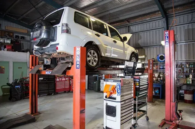 White SUV lifted on a red car hoist inside an auto repair garage, with tools and equipment nearby — Auto Inspections & Road Services N.T. in Woolner, NT