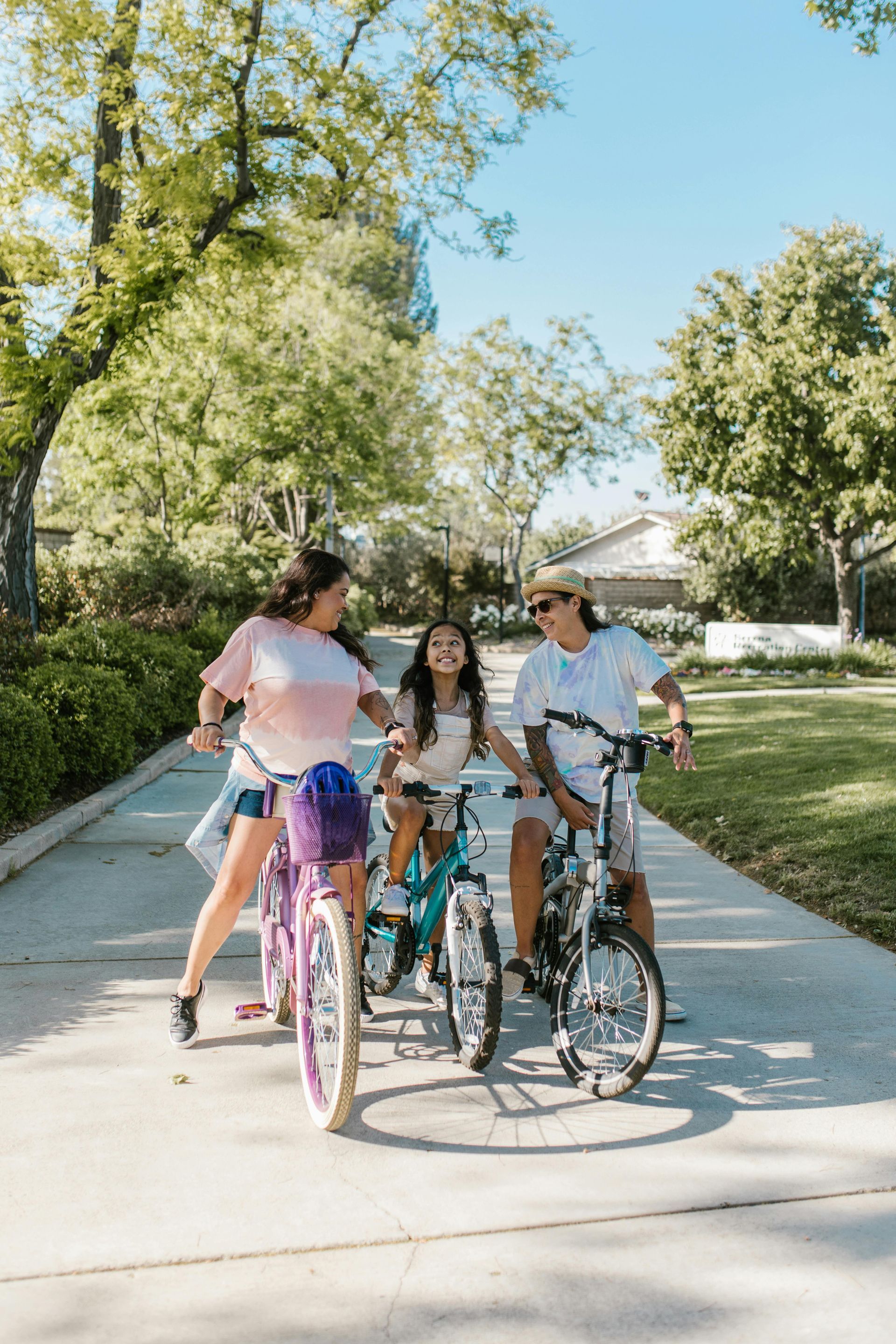 Family of three riding bikes on a paved path on a sunny day.