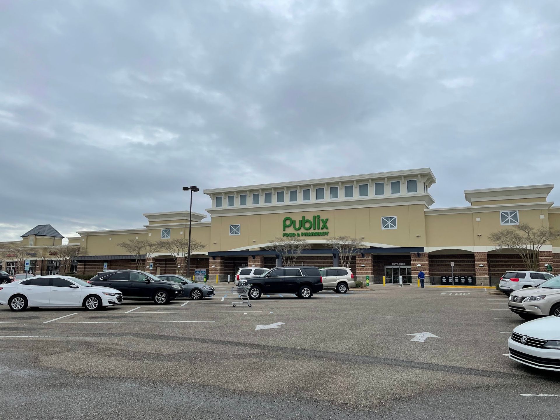 Publix supermarket entrance with cars parked in front on a cloudy day.