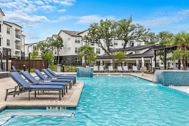 Swimming pool with blue lounge chairs, apartments in the background on a sunny day.