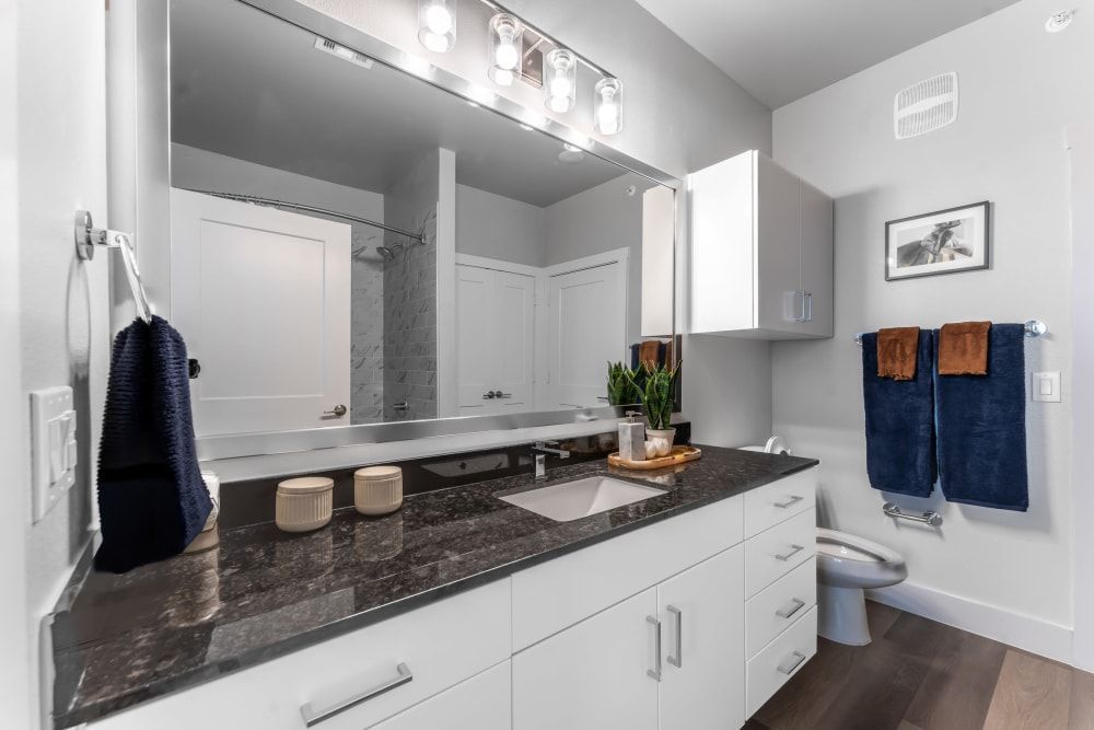 Apartment bathroom with two sinks, a toilet, and a large mirror at The Gabriel, which offers Leander apartments for rent.