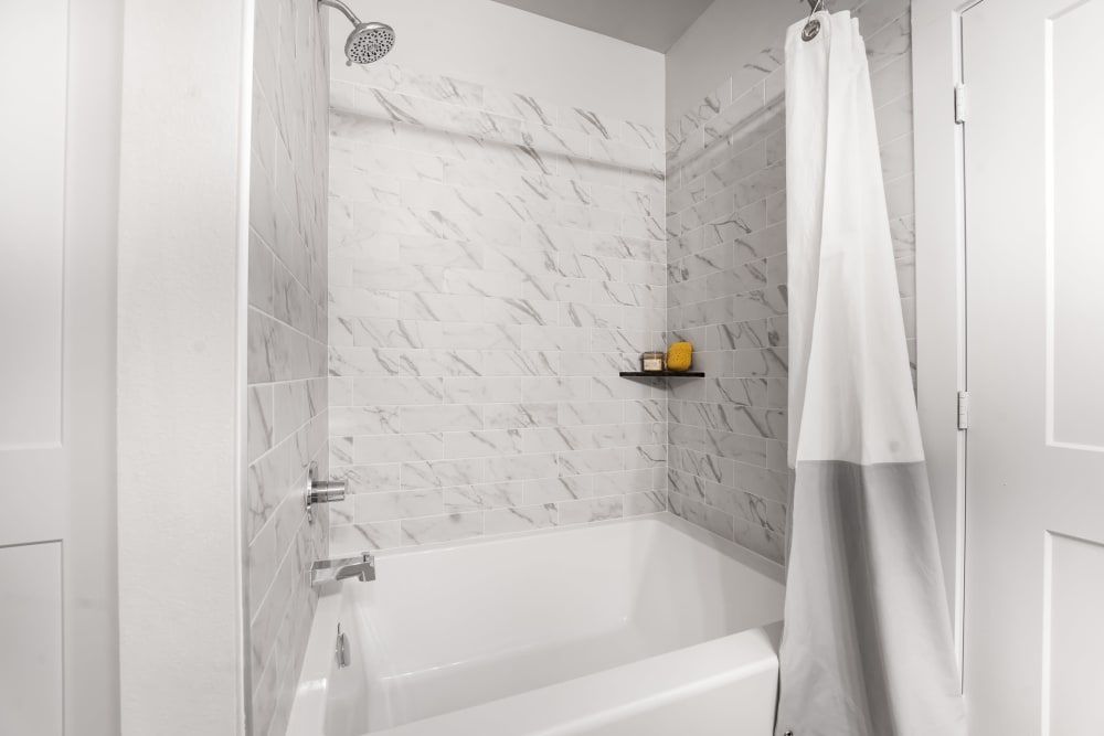 A bathroom with a bathtub/shower, and marble walls at The Gabriel, which offers Leander apartments for rent.
