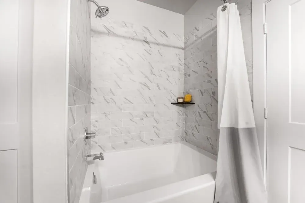 A bathroom with a bathtub/shower, and marble walls at The Gabriel, which offers Leander apartments for rent.