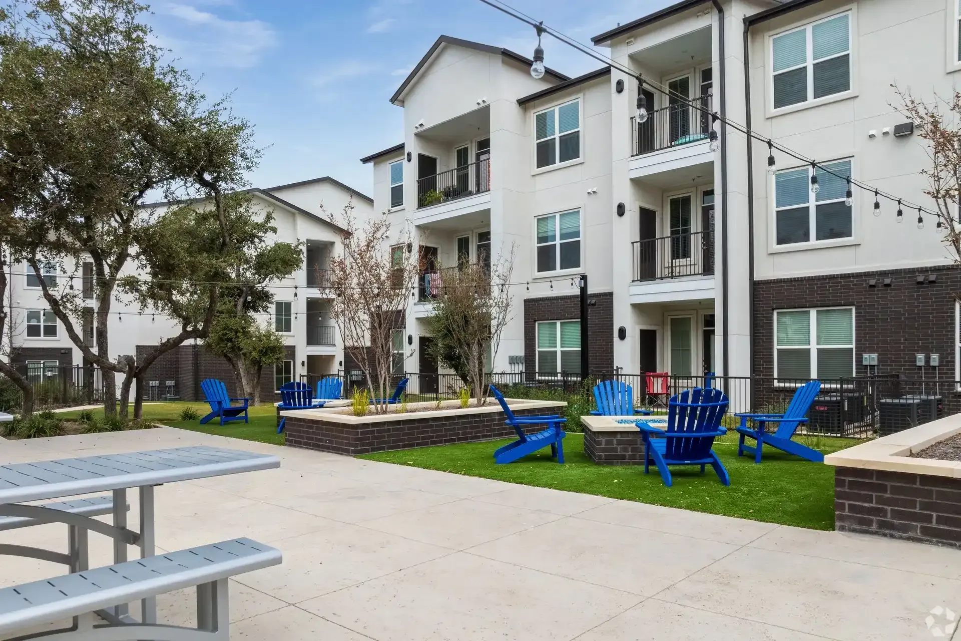 A large apartment building with a courtyard featuring a picnic table and chairs in front of it at The Gabriel, which offers new apartments near Cedar Park.
