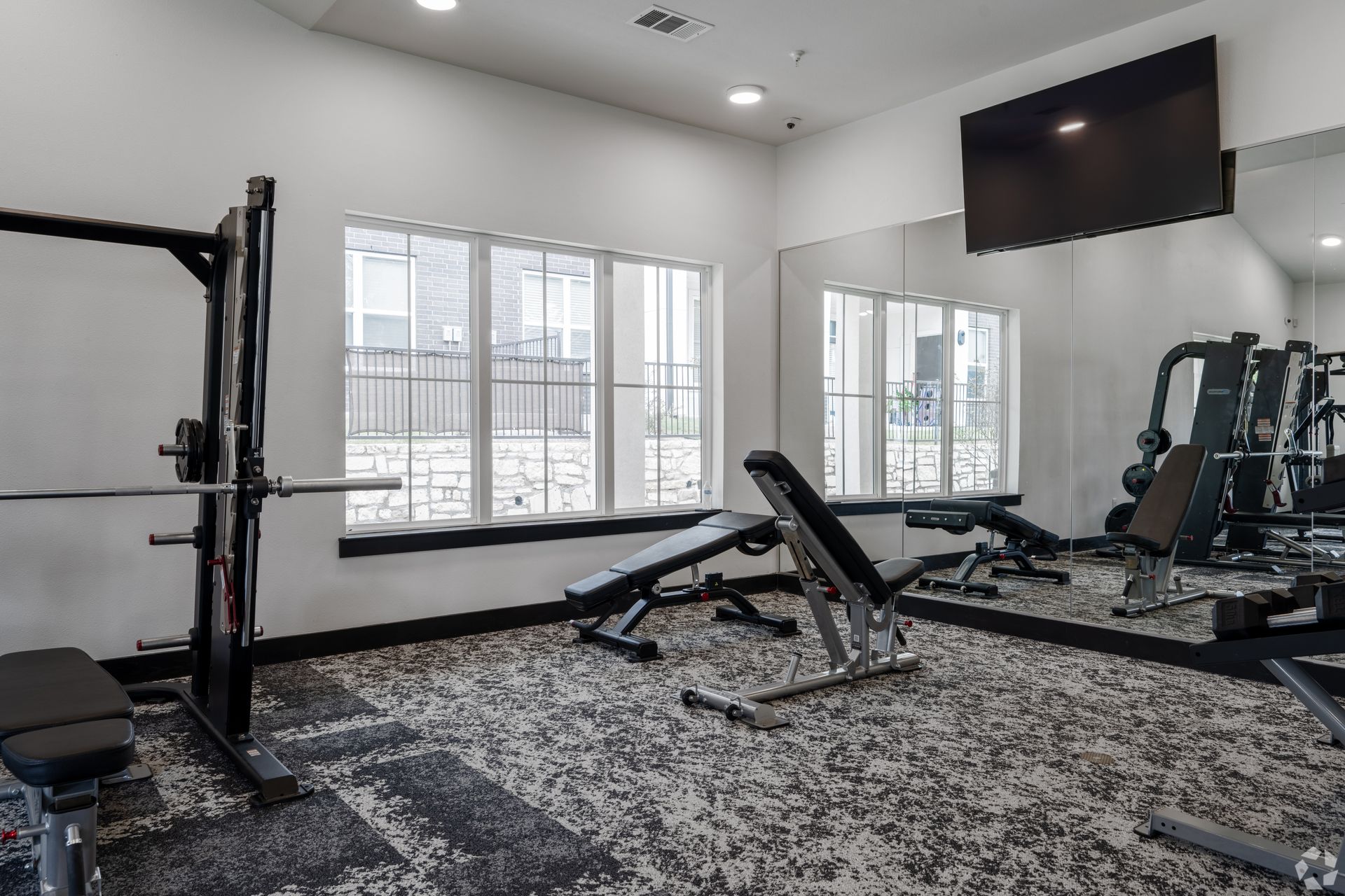 A gym with a lot of equipment, an oversized mirror, and a flat-screen TV on the wall at The Gabriel, which offers Leander, TX apartments for rent near Northtech Business Center.